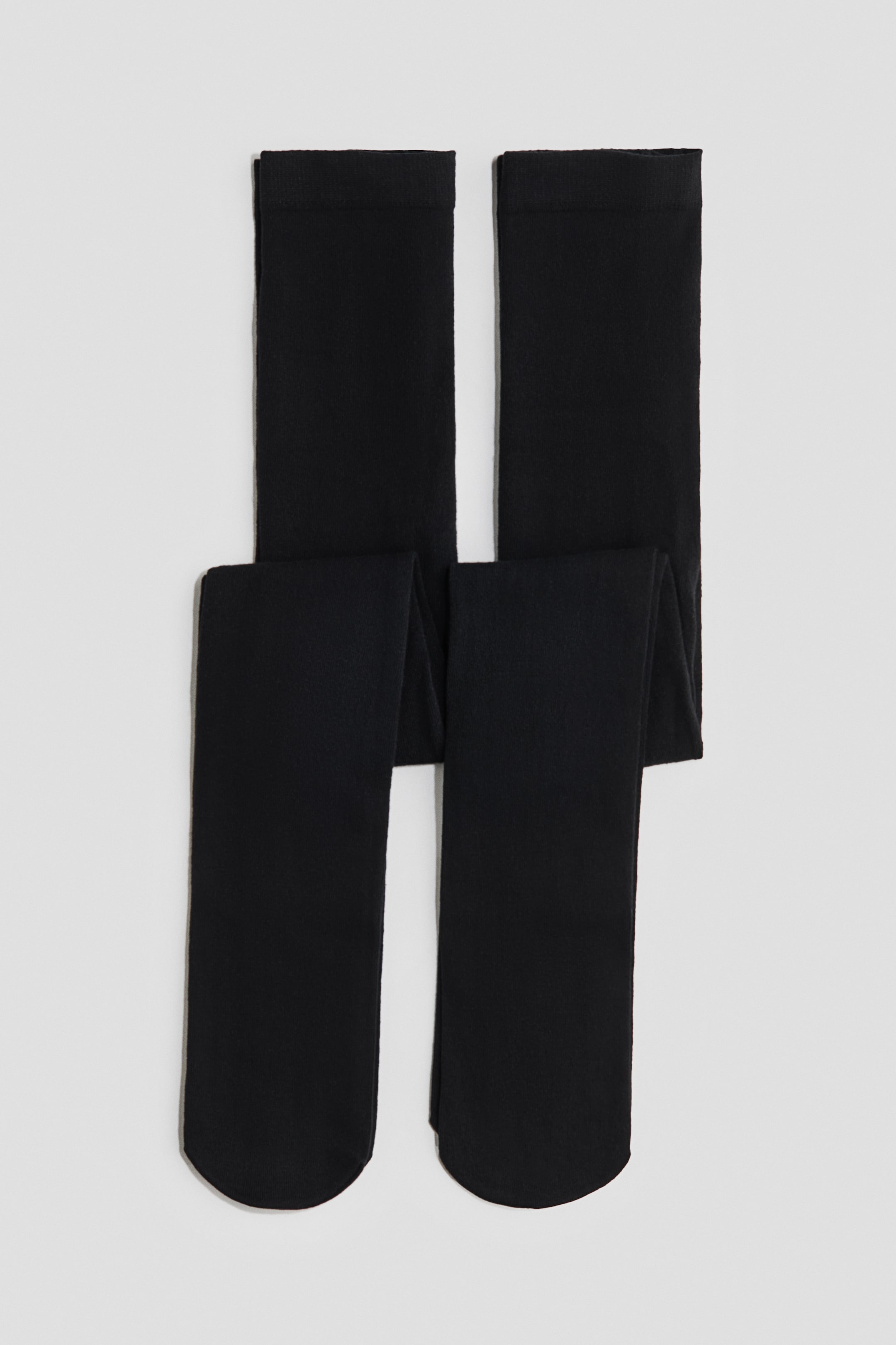 Größeres Bild ansehen: Schwarze Strumpfhosen aus einem fein gestrickten Baumwollmix liegen flach in einer Frontansicht, horizontal gefaltet, wobei die Beine gerade nach unten hängen. Die Strumpfhosen zeigen eine einheitliche, blickdichte schwarze Farbe mit einer weichen, matten Textur.