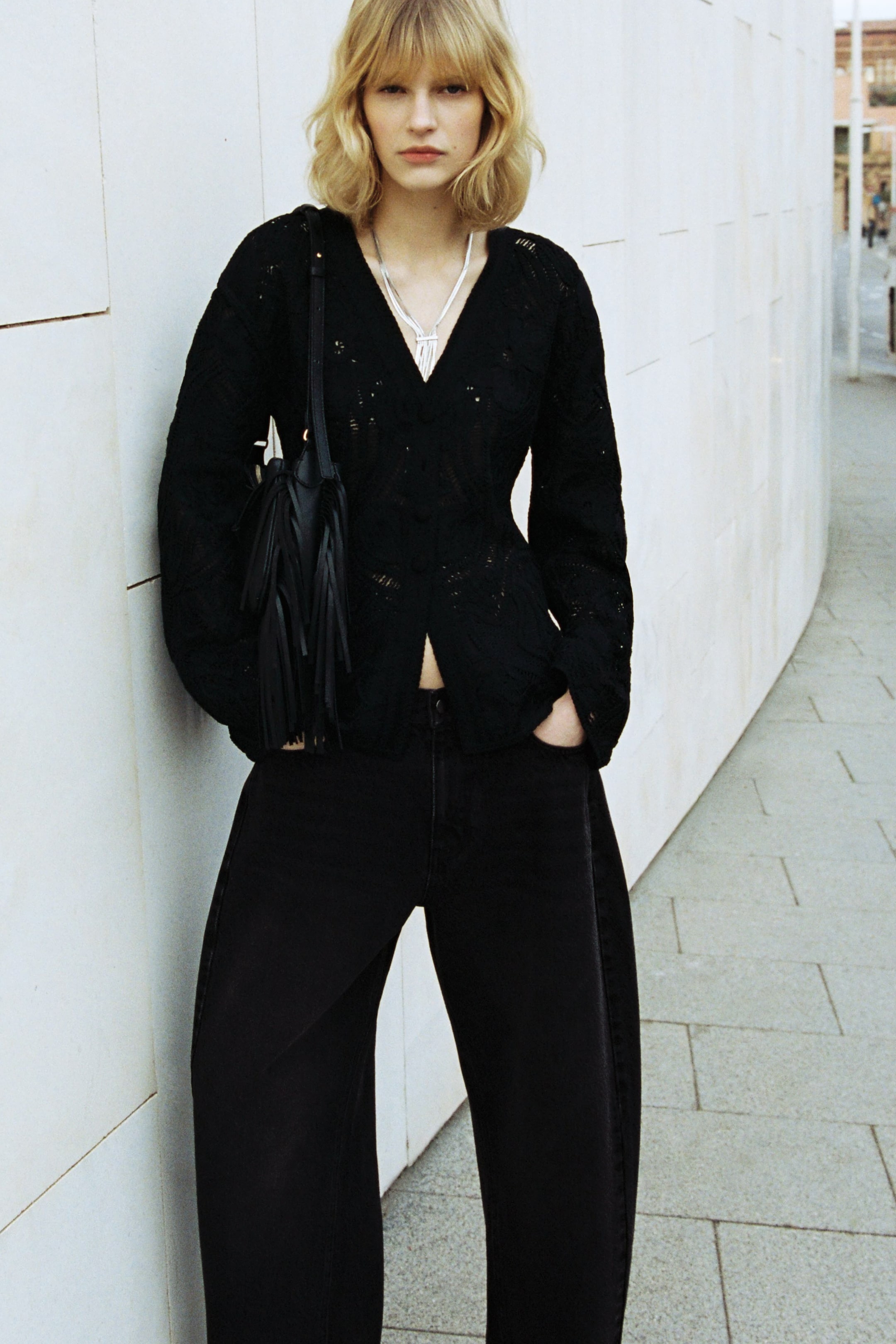 View larger image: A black V-neck top with an openwork texture and long, relaxed sleeves is paired with black wide-leg pants. The top features a single-button closure at the waist, revealing a small section of the midriff.