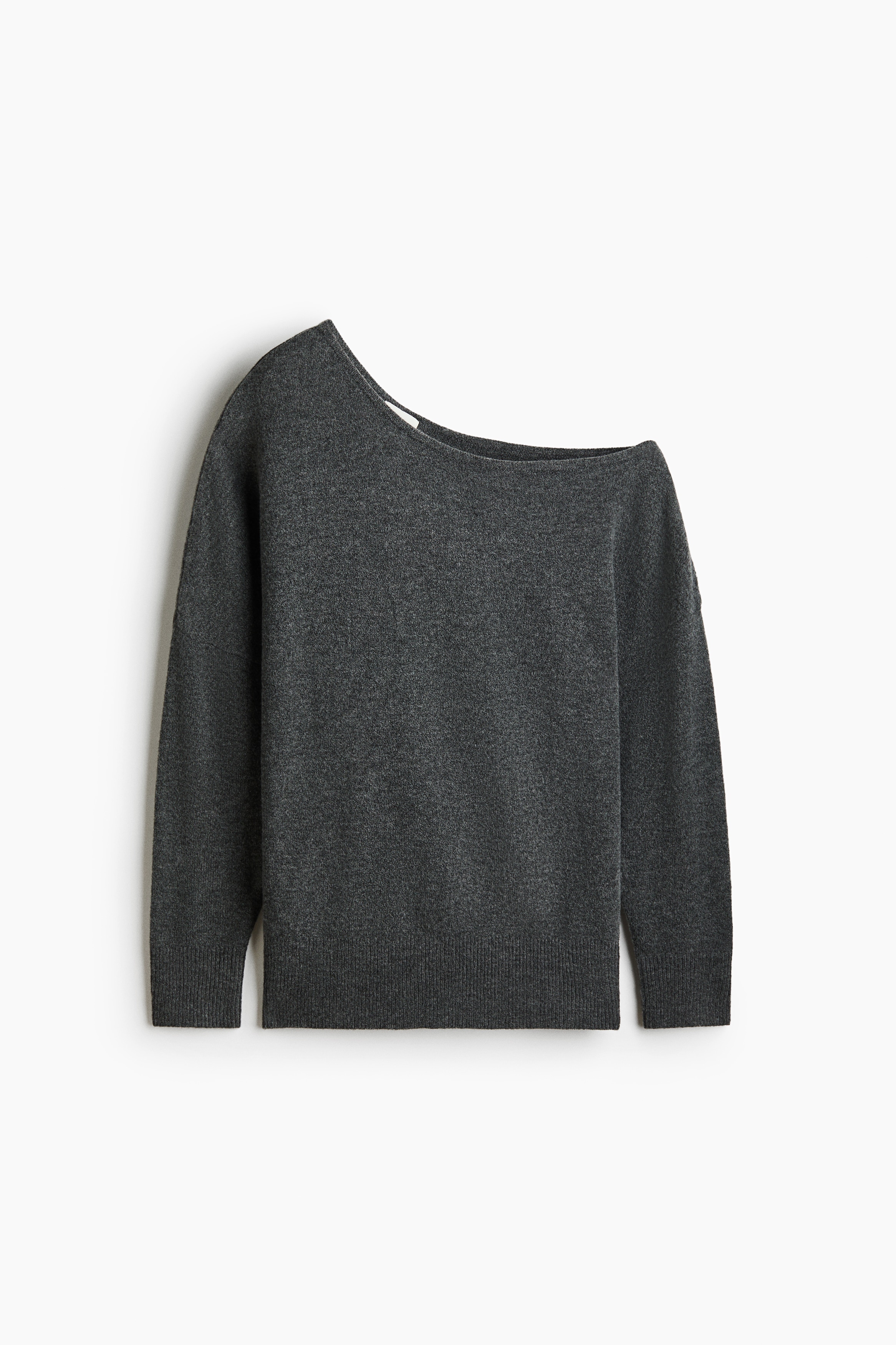 A dark grey, fine-knit sweater featuring an asymmetrical off-the-shoulder neckline and low dropped shoulders is being worn by the model. The sweater has extra-long sleeves with ribbed cuffs and is styled with light blue jeans.
