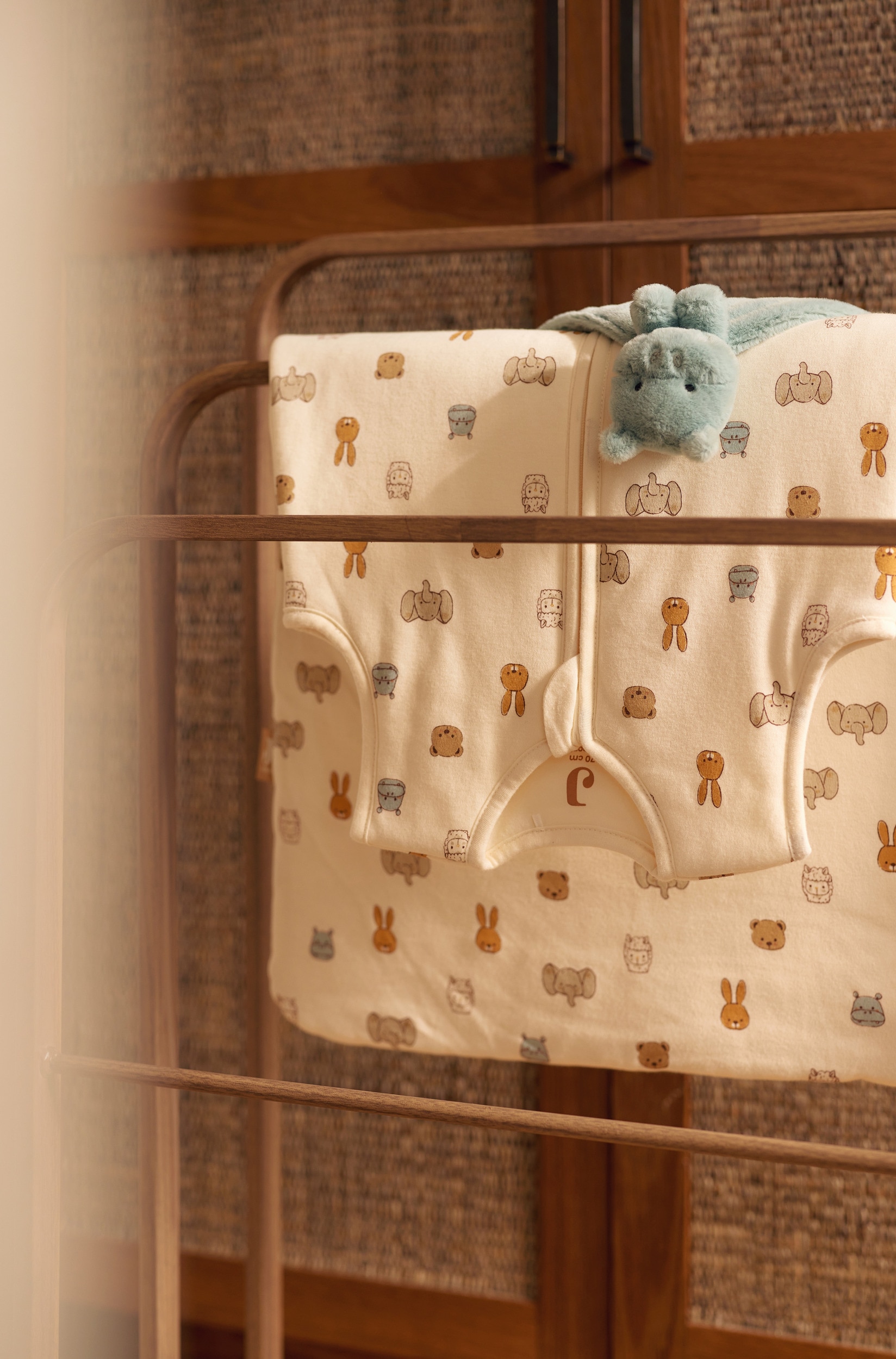 Ein Ã¤rmelloser Babyschlafsack liegt flach und nach vorne ausgerichtet und zeigt einen cremeweiÃen Stoff mit einem Allover-Print aus kleinen Zeichentiergesichtern in gedeckten ErdtÃ¶nen. Der Schlafsack verfÃ¼gt Ã¼ber einen runden Ausschnitt und einen durchgehenden, mittig verlaufenden ReiÃverschluss auf der Vorderseite.