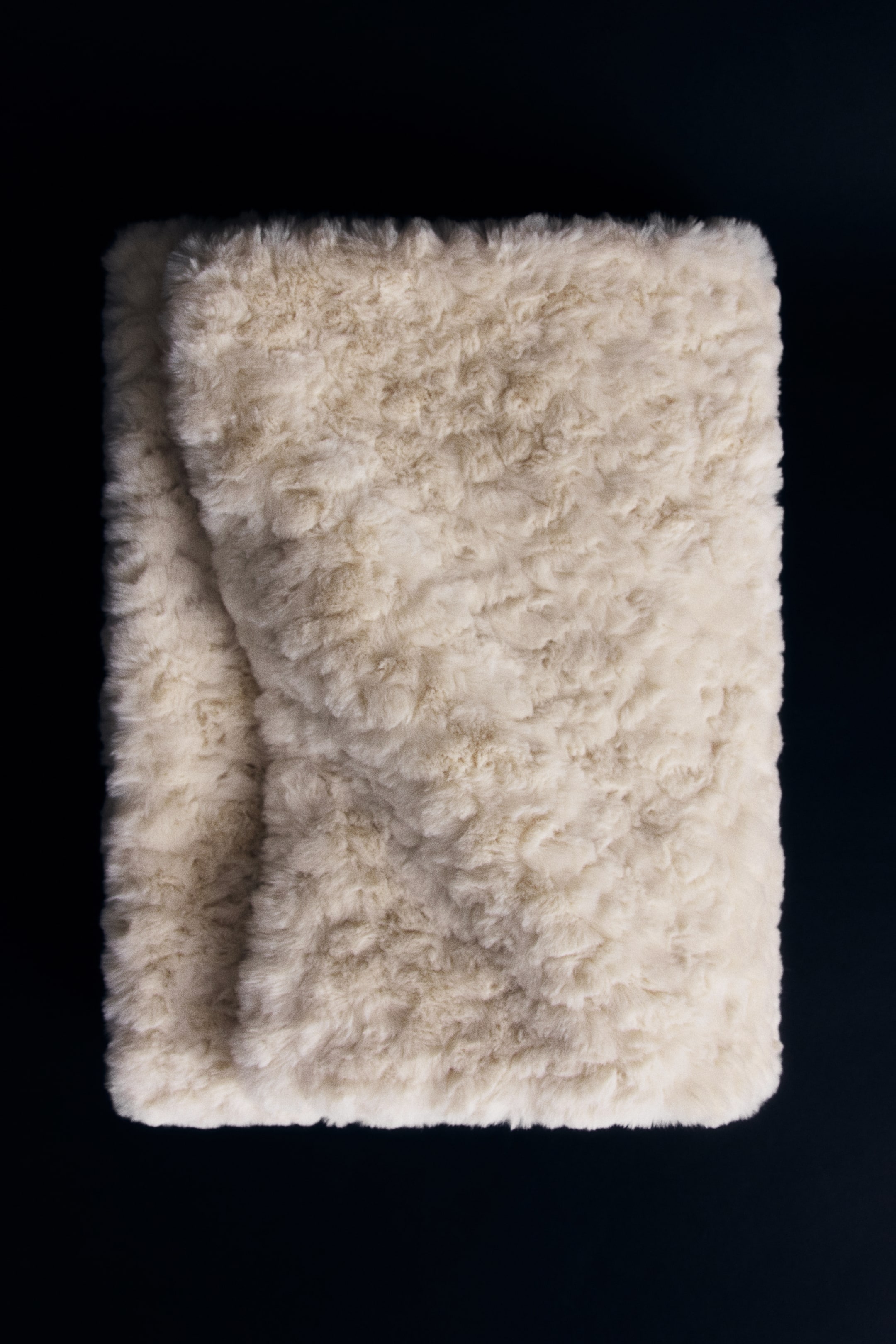 View larger image: A cream-coloured blanket in soft, fluffy fabric is lying folded, displaying its dense, wavy pile fleece texture on its structured front.