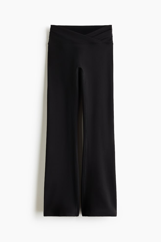 Pantalones negros de pierna ancha con una pretina alta cruzada y un sutil fruncido. Cada pierna del pantalón presenta una abertura vertical prominente en la parte delantera, que se extiende desde el dobladillo hacia arriba. - 1