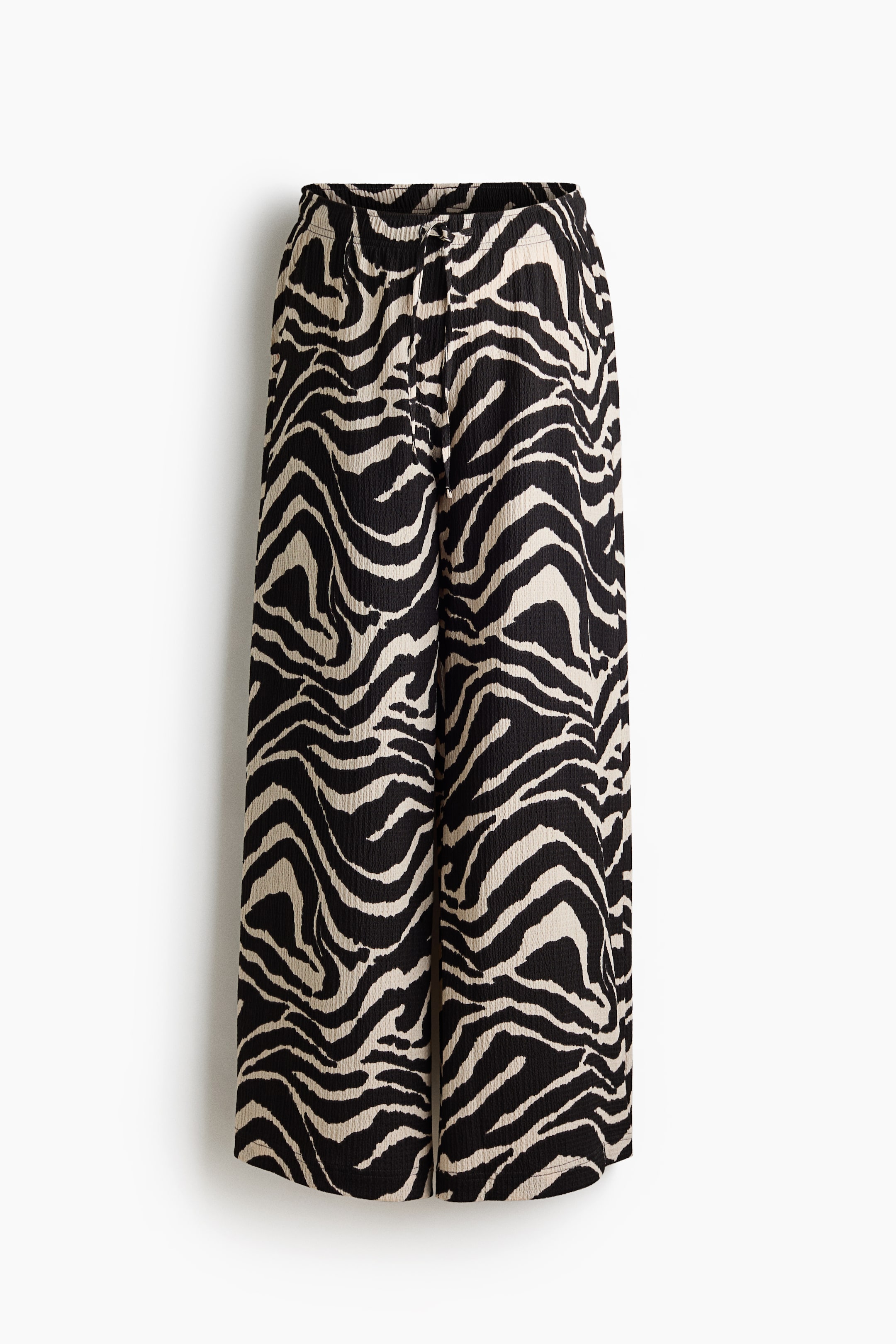 View larger image: The pants are shown from the front, showcasing a loose fit and wide legs. They feature a black and beige zebra print on woven fabric, with a low-rise waist that includes covered elastic and a slim drawstring.