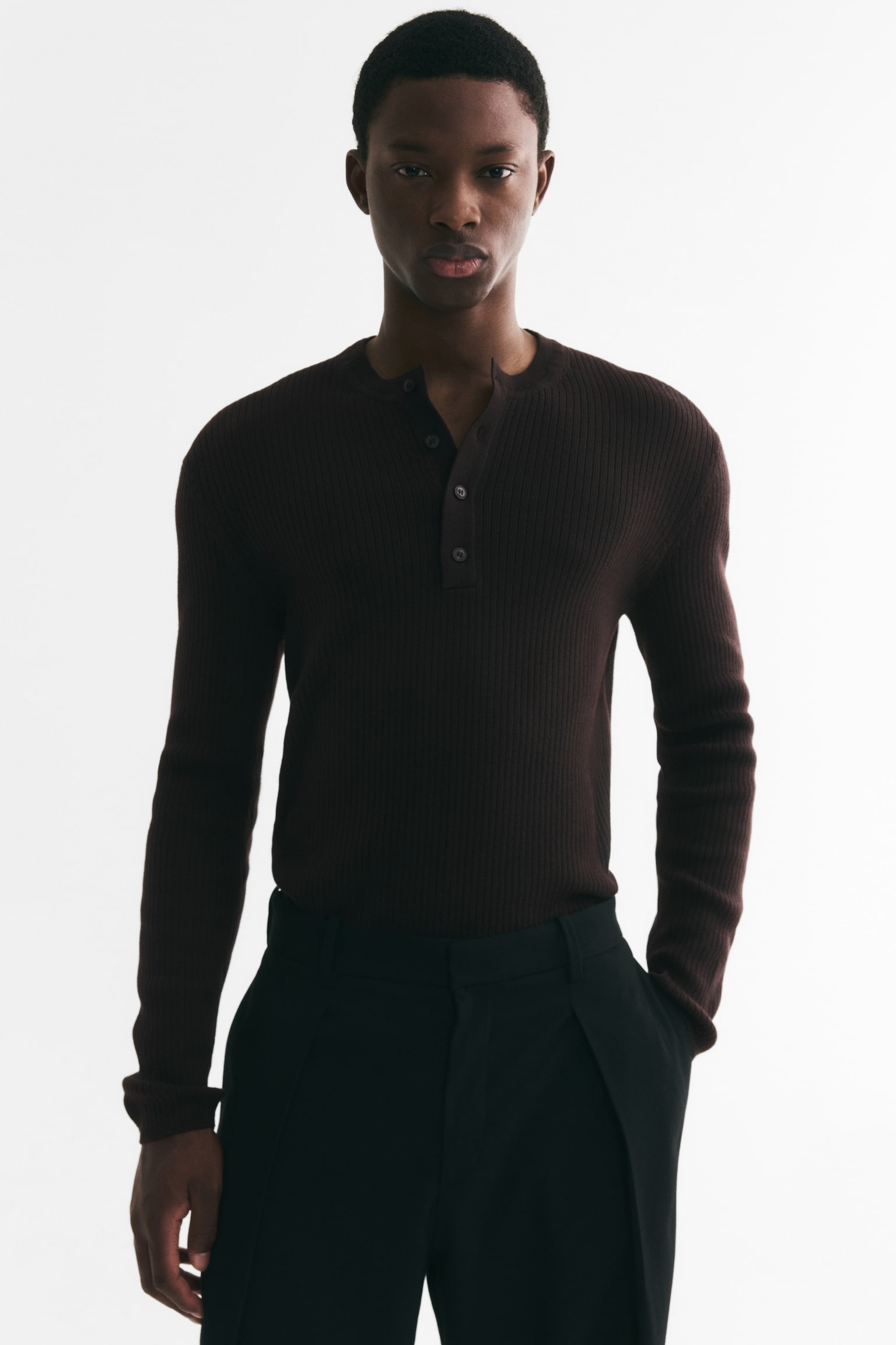 A dark brown long-sleeved henley shirt is facing front, showcasing a ribbed knit texture throughout the body and long sleeves. It features a round neckline leading to a four-button placket with dark, round buttons. The long sleeves end in finished cuffs, while the bottom hem is also neatly finished. - 1