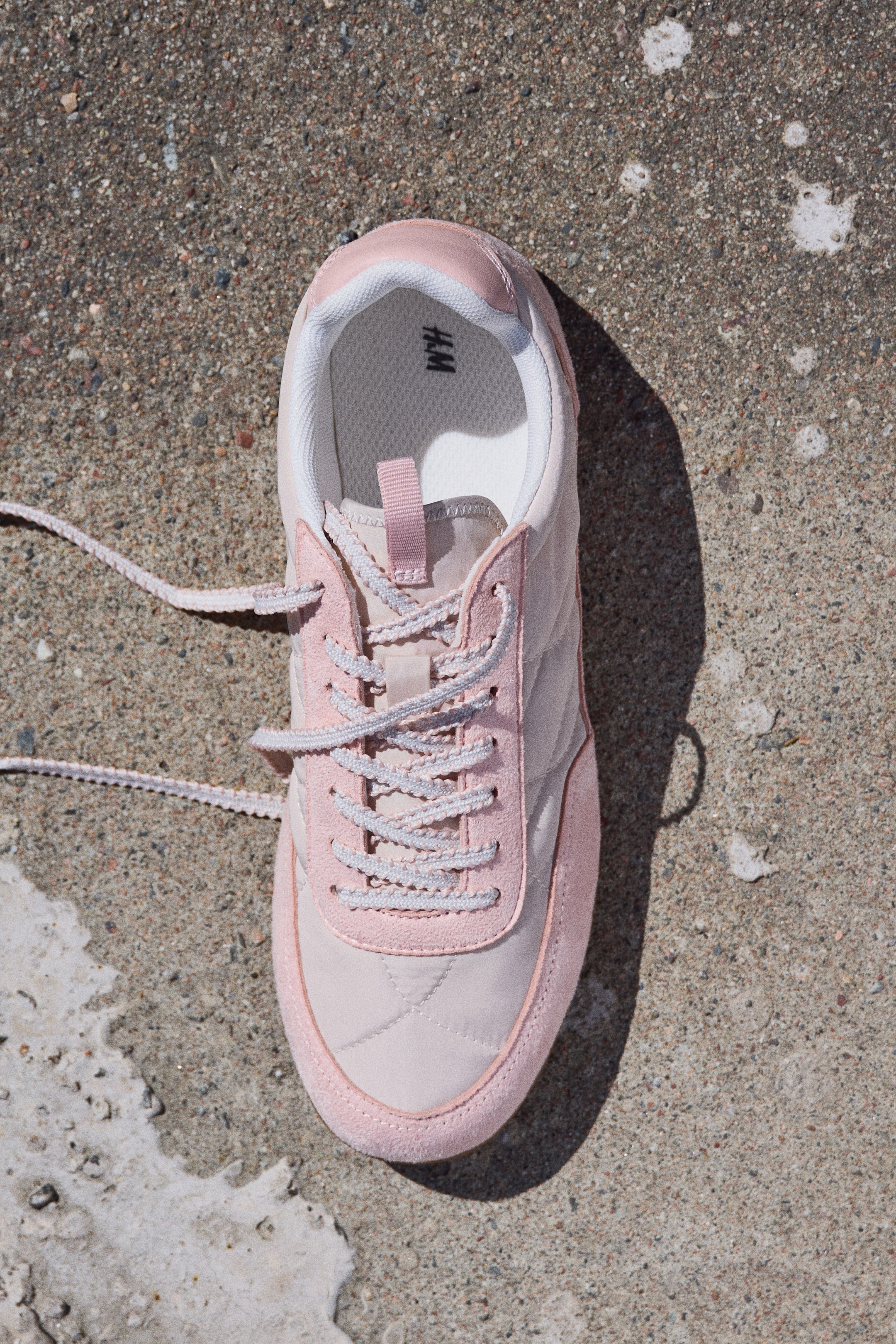 View larger image: A low-profile sneaker is shown from above, facing forward. It boasts a light pink quilted nylon upper with darker pink coated fabric sections that have a soft, napped finish. Light pink laces thread through eyelets at the front, and the opening reveals a padded edge with mesh lining and an H&M logo on the insole.