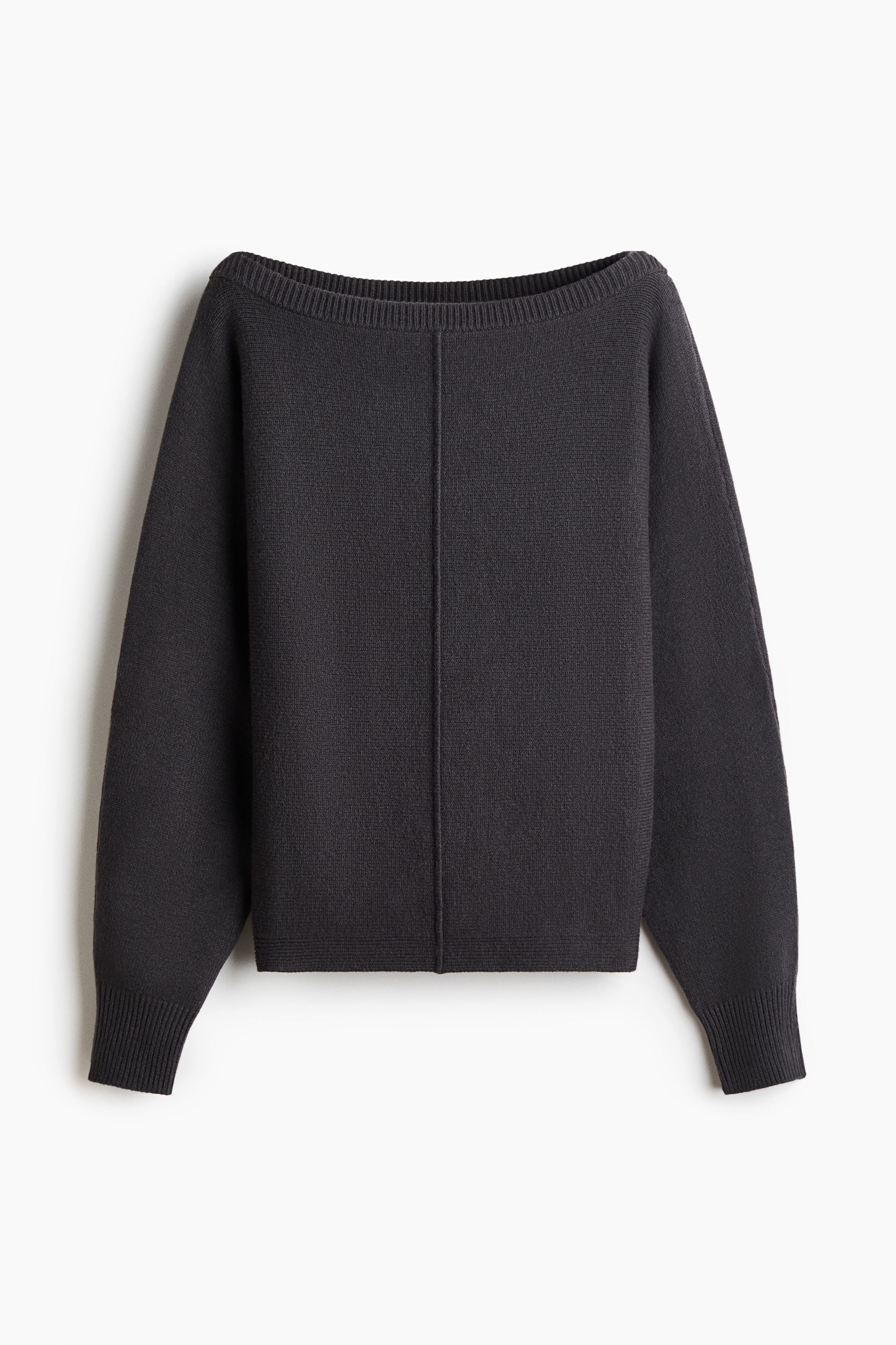 Een donkergrijze gebreide trui met een boothals met ribboord en een zichtbare naad aan de voorkant wordt door het model gedragen, licht off-shoulder gestyled. De trui met lange mouwen wordt gecombineerd met een beige broek, een tweede grijze knit die om de taille is geknoopt, en een zwarte clutch die onder de arm wordt gedragen.