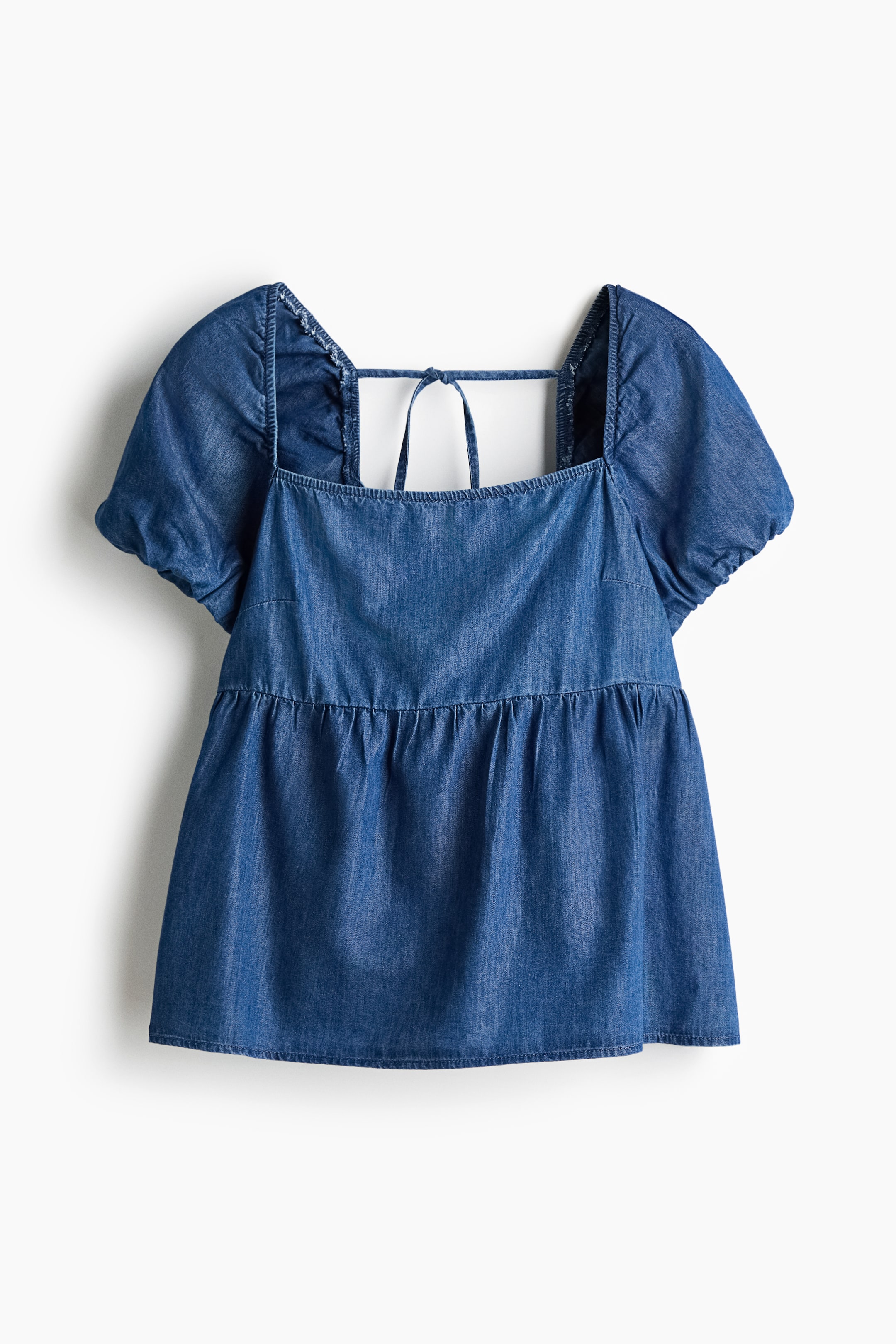View larger image: A blue denim top, presented in a FRONT view, is featuring a square neckline with covered elastication over the shoulders and short puff sleeves. It is designed with an open back with narrow ties at the top, covered elastication below, a gathered seam under the bust, and a gently flared hem.