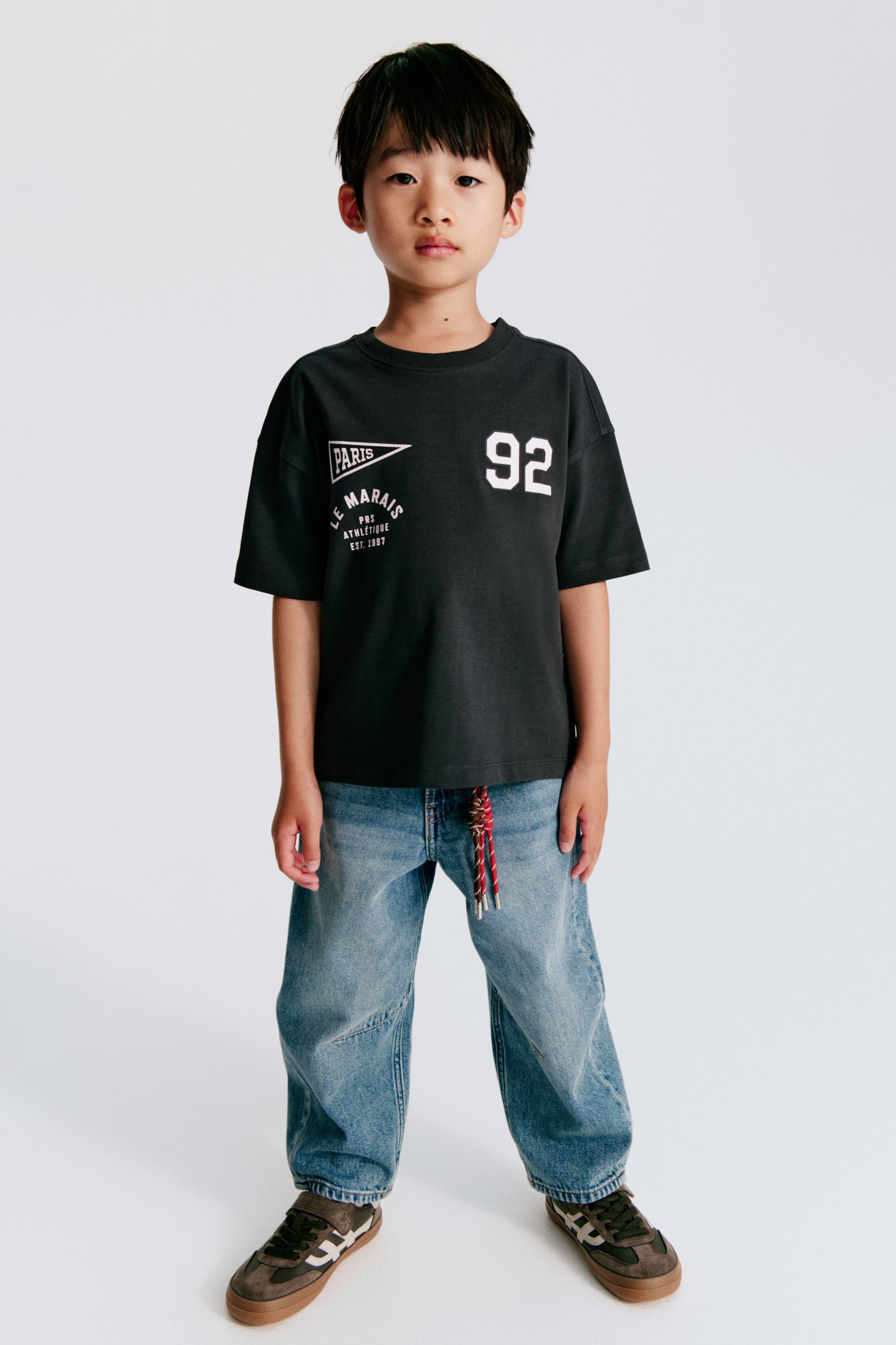 De lichtblauwe denim jeans zijn voorzien van een knoop- en ritssluiting aan de voorkant, een elastische tailleband aan de achterkant en riemlussen. Ze hebben twee gebogen voorzakken, een muntzakje en stikdetails die lijken op kniestukken op de wijde, cropped pijpen. - 1