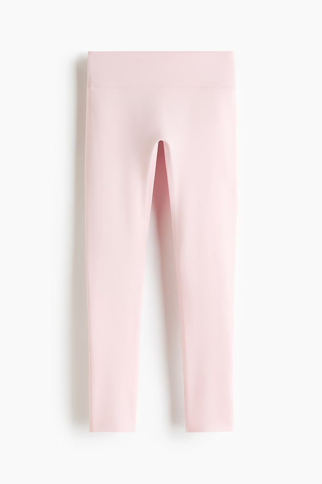 SoftMove sports leggings in light pink are laid flat, showcasing a front view. They feature a wide, high-rise waistband and smooth fabric, with the legs slightly apart at the crotch. - 1