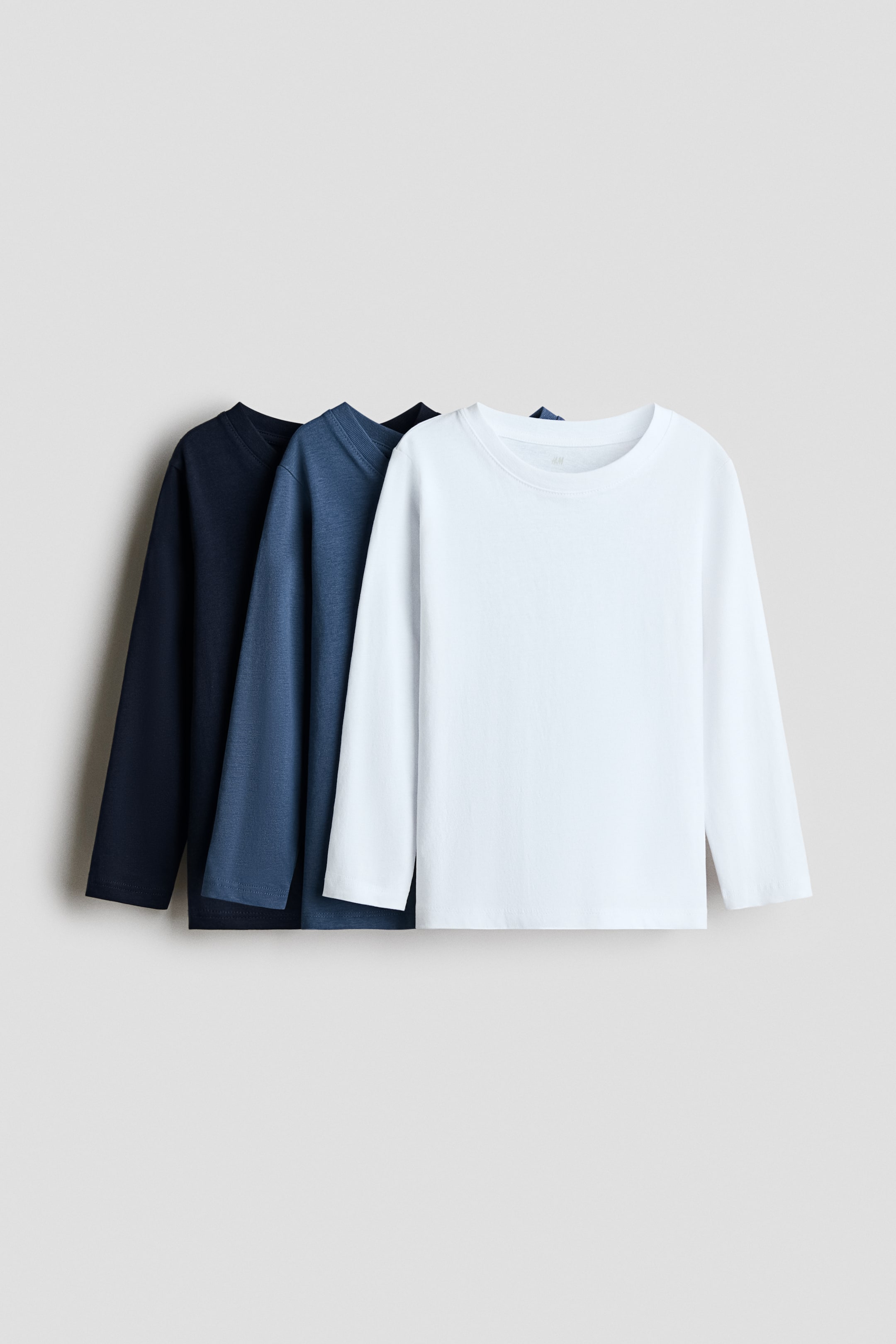 View larger image: Three long-sleeved t-shirts are showcased, layered from front to back. The front white shirt, middle blue shirt, and back dark blue shirt all feature round, ribbed necklines and long sleeves.