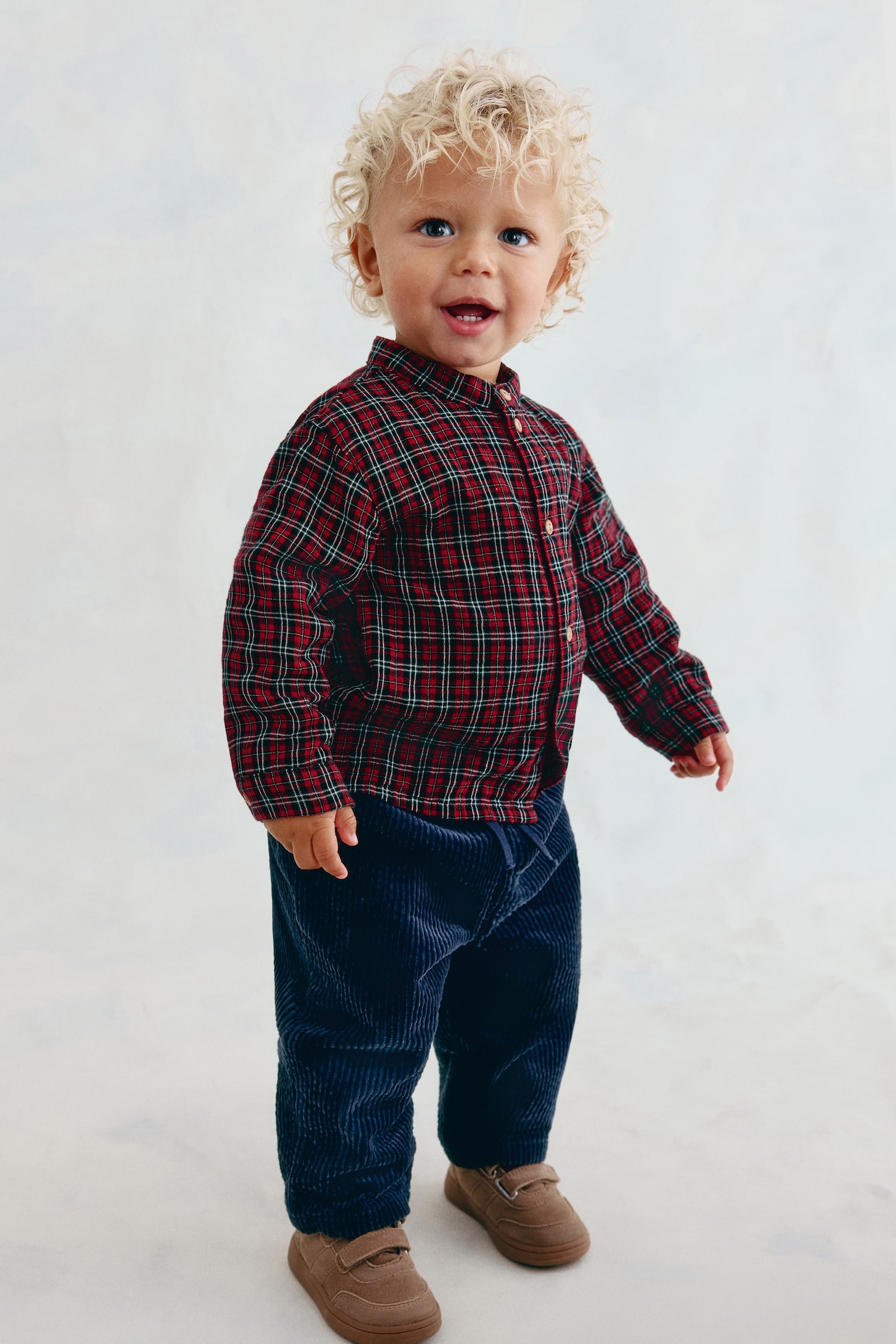 Una camicia a quadri, caratterizzata da un motivo in rosso scuro, nero e bianco, presenta la sua vista frontale. È progettata con un colletto a fascia e una pattina frontale fissata da quattro bottoni di colore chiaro, e le sue maniche lunghe terminano con orli semplici. - 1