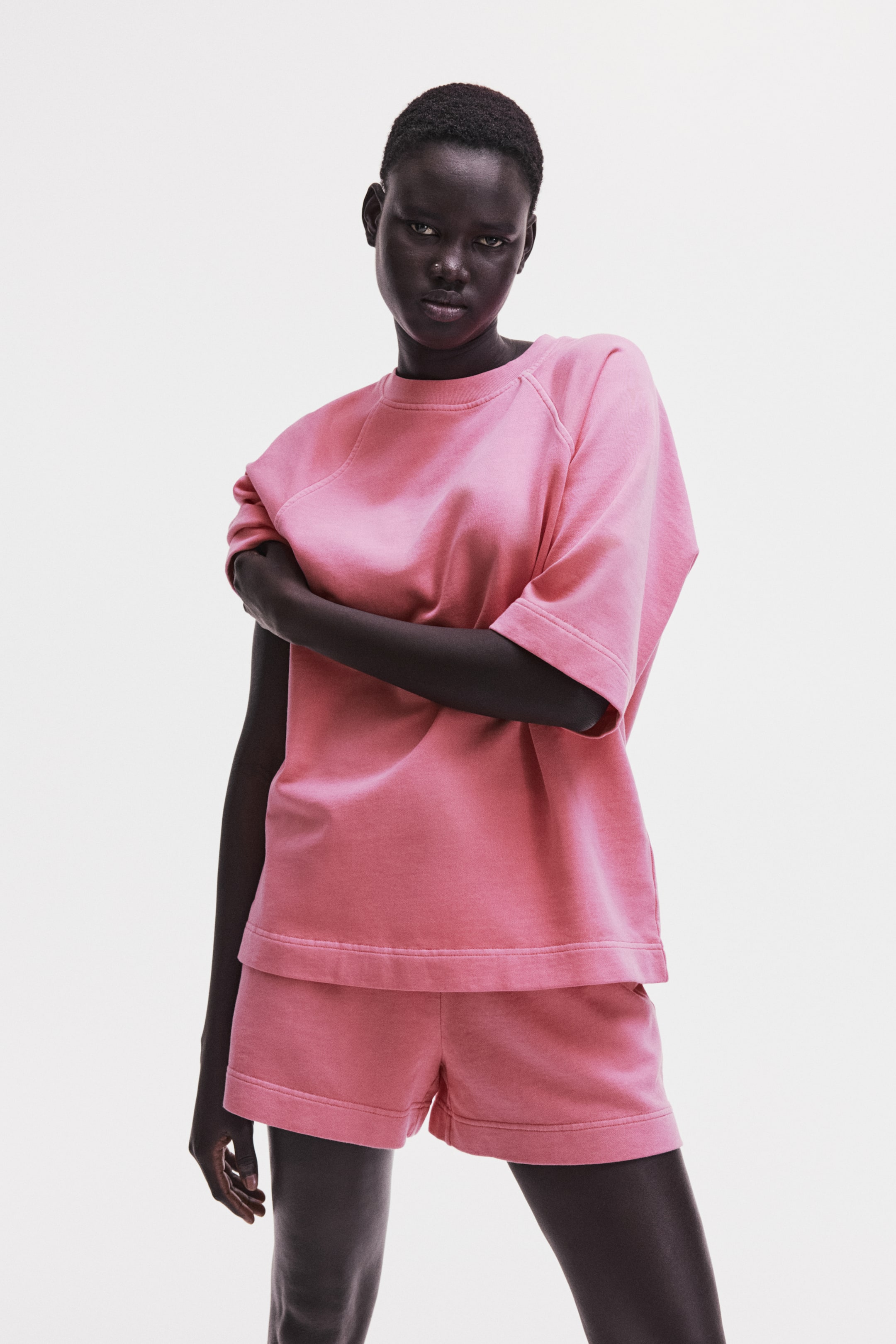 View larger image: A pink short-sleeved T-shirt and matching shorts set is shown from the front. The T-shirt features raglan sleeves, a crew neck, a relaxed fit, and a wide banded hem. The coordinating shorts also have a relaxed fit and a wide banded hem.