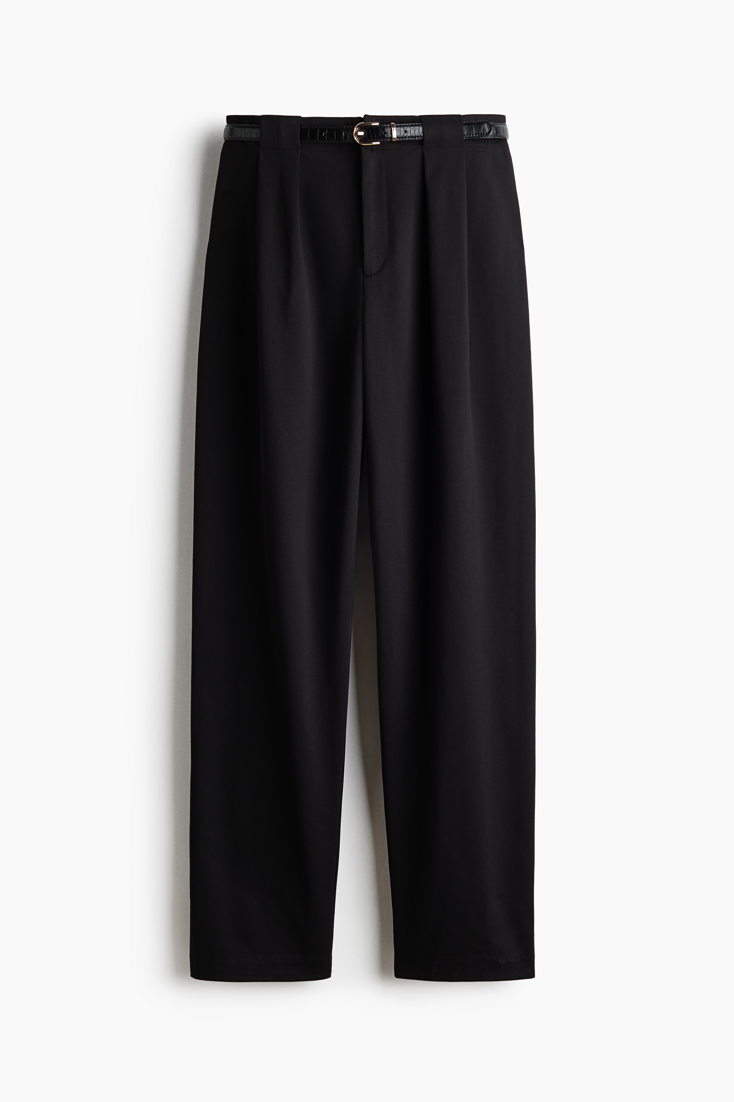Le mannequin porte un pantalon noir ajusté en jersey texturé, doté de plis à la taille haute et de jambes fuselées. Le pantalon est porté avec une ceinture noire fine à boucle métallique et un débardeur noir rentré.