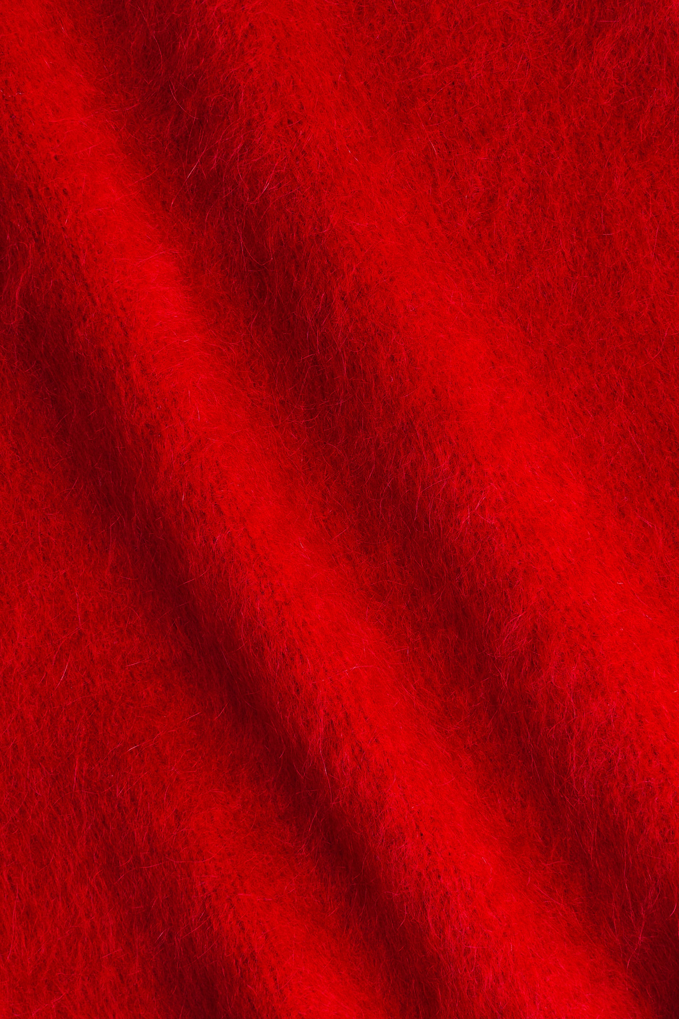 Ampliar la imagen: Una tela de punto suave de un suéter de ajuste holgado, que contiene mohair y lana, se presenta en un color rojo vibrante, exhibiendo una textura peluda y pliegues sutiles.