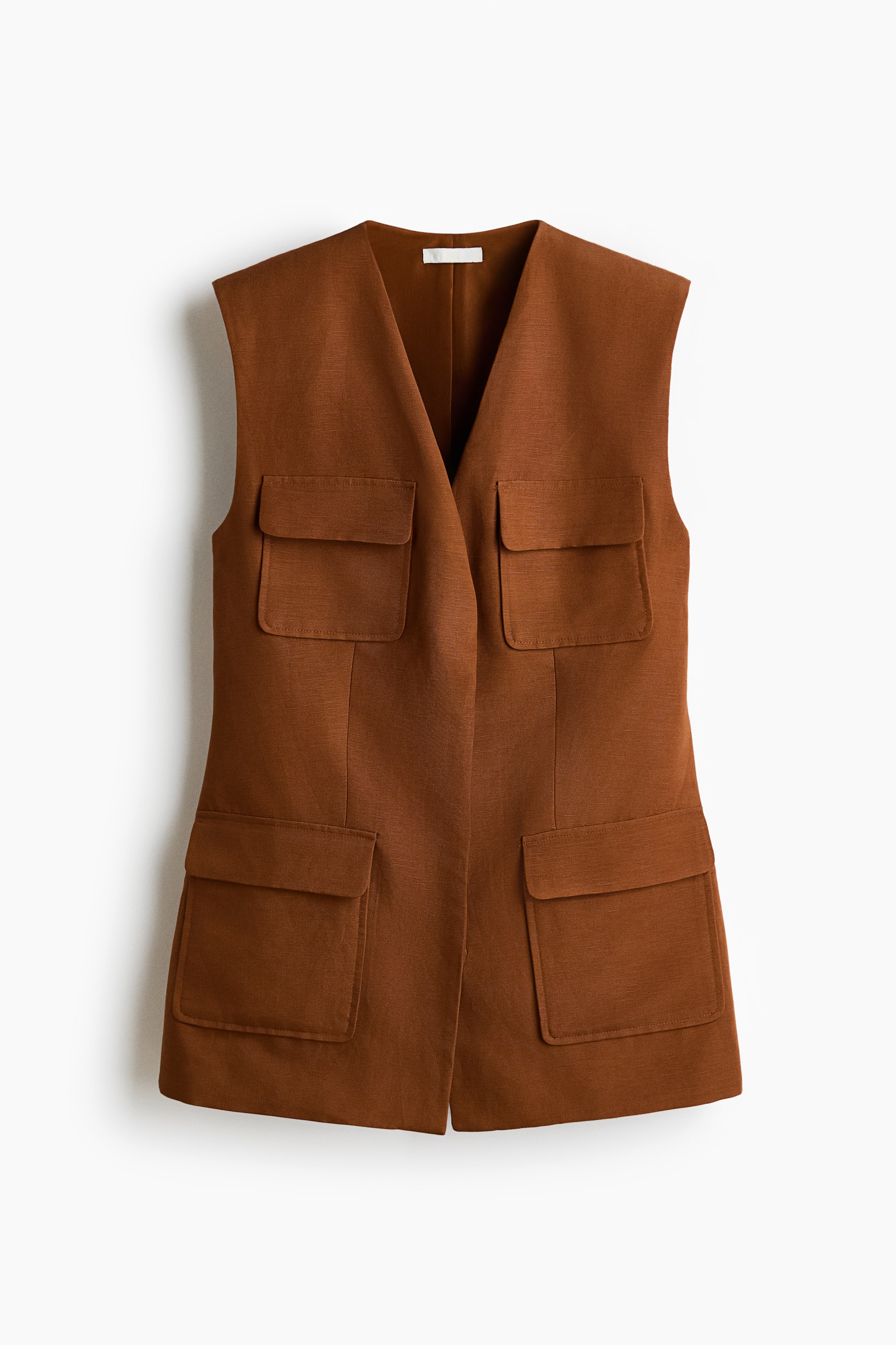 Ver imagem maior: Um colete castanho sem mangas é visível de frente, feito de um tecido texturizado. Apresenta um decote em V e quatro bolsos de aba, com dois colocados na parte superior do peito e dois posicionados perto da bainha.