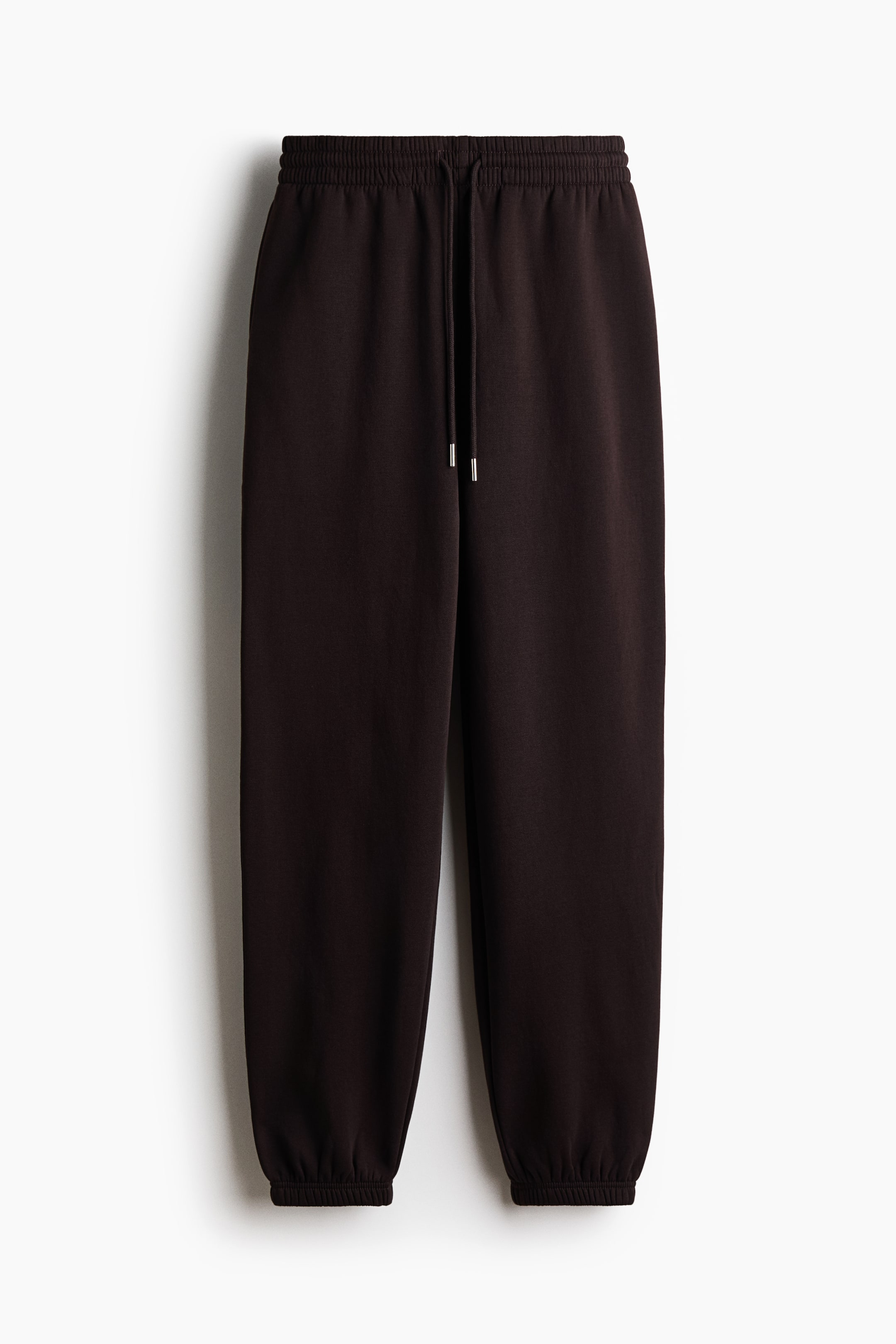 View larger image: A pair of dark brown track pants is shown from the front, featuring a high-rise, covered elastic waistband with a matching drawstring and tapering down to gathered elastic cuffs.