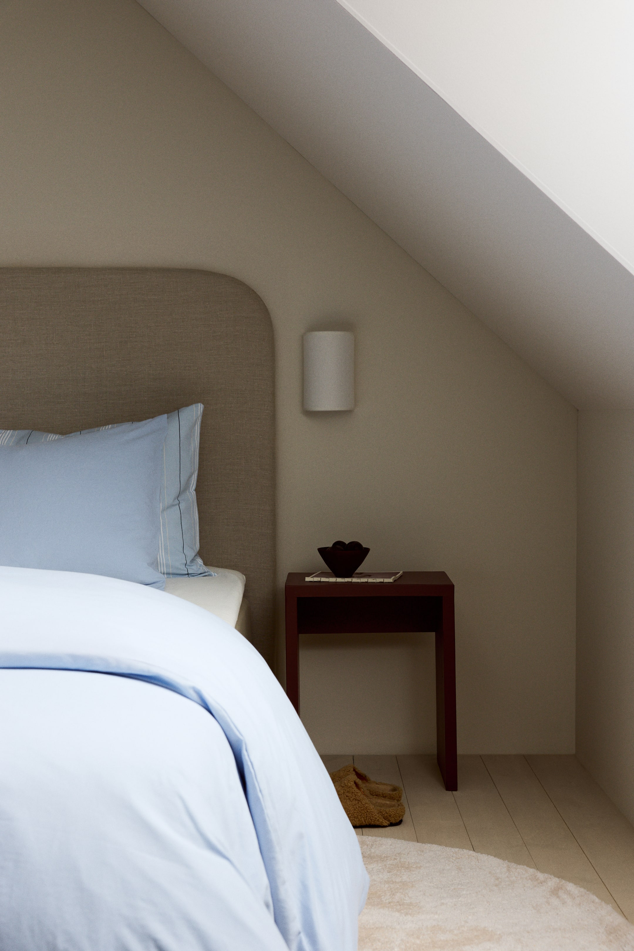 View larger image: A light blue duvet cover is neatly draped over the bed, while a matching light blue pillowcase, featuring thin white and dark blue vertical stripes along its right side, rests against a fabric headboard.