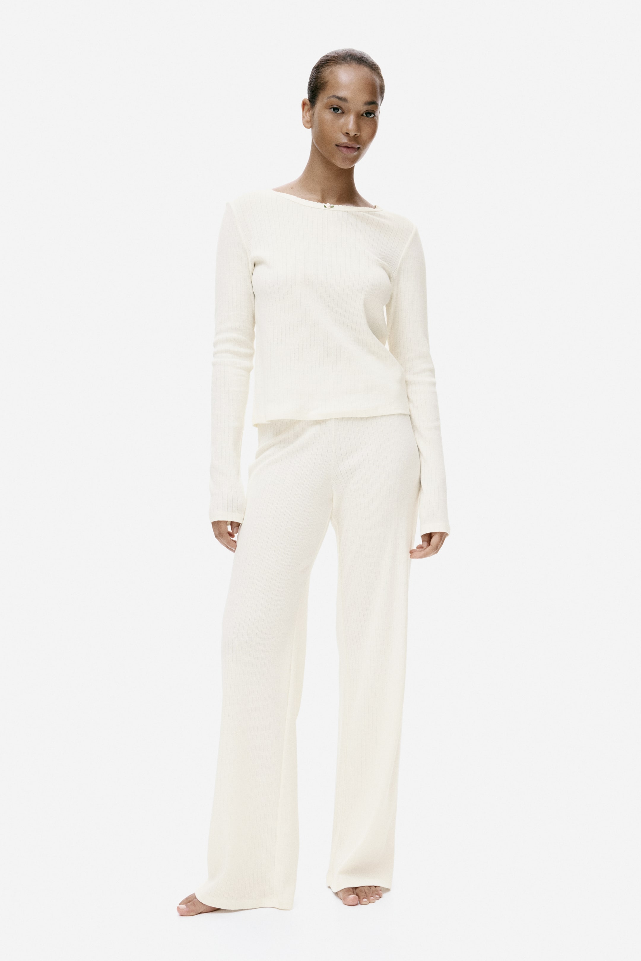 View larger image: A cream ribbed-knit matching set is presented, consisting of a long-sleeved boat-neck top with a small decorative detail at the neckline and wide-leg trousers.