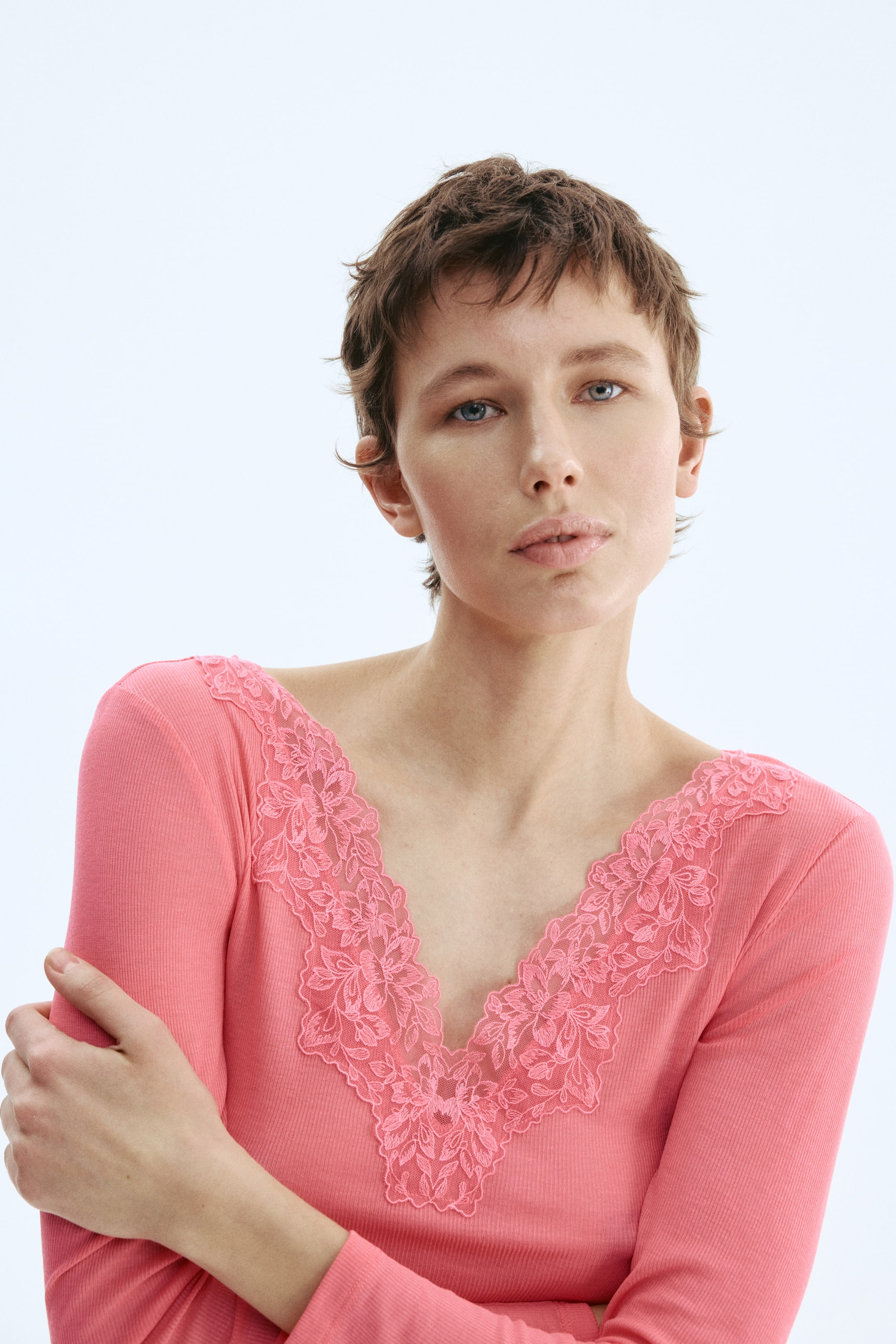 View larger image: A coral-pink long-sleeved top is showcased, featuring a ribbed knit texture. Its V-neckline is adorned with a matching intricate floral lace trim.