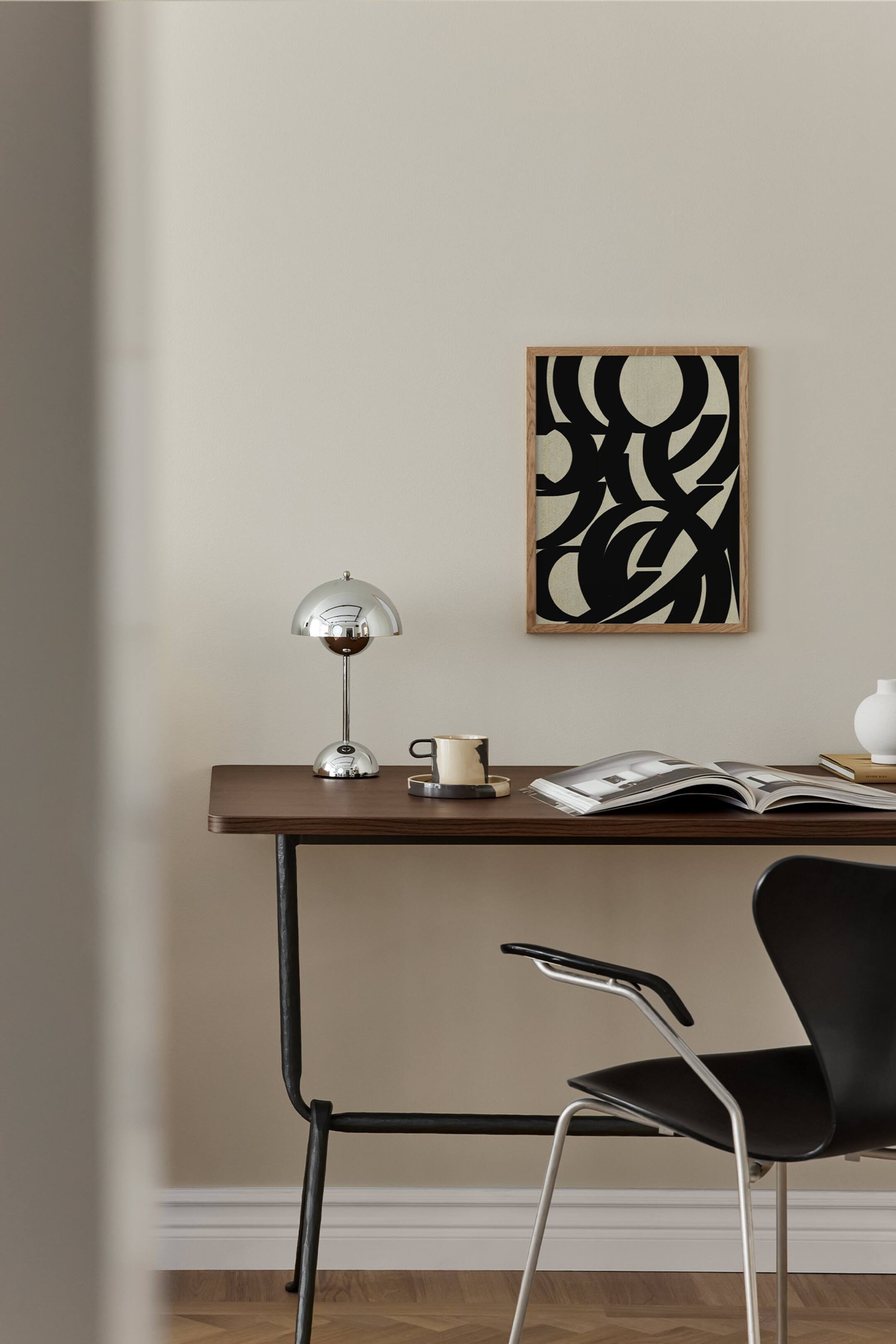 Se større billede: Et rektangulært indrammet kunsttryk, der viser et abstrakt sort og beige grafisk design med krydsende buede linjer, indrammet i en lys egetræsfarvet træramme.
