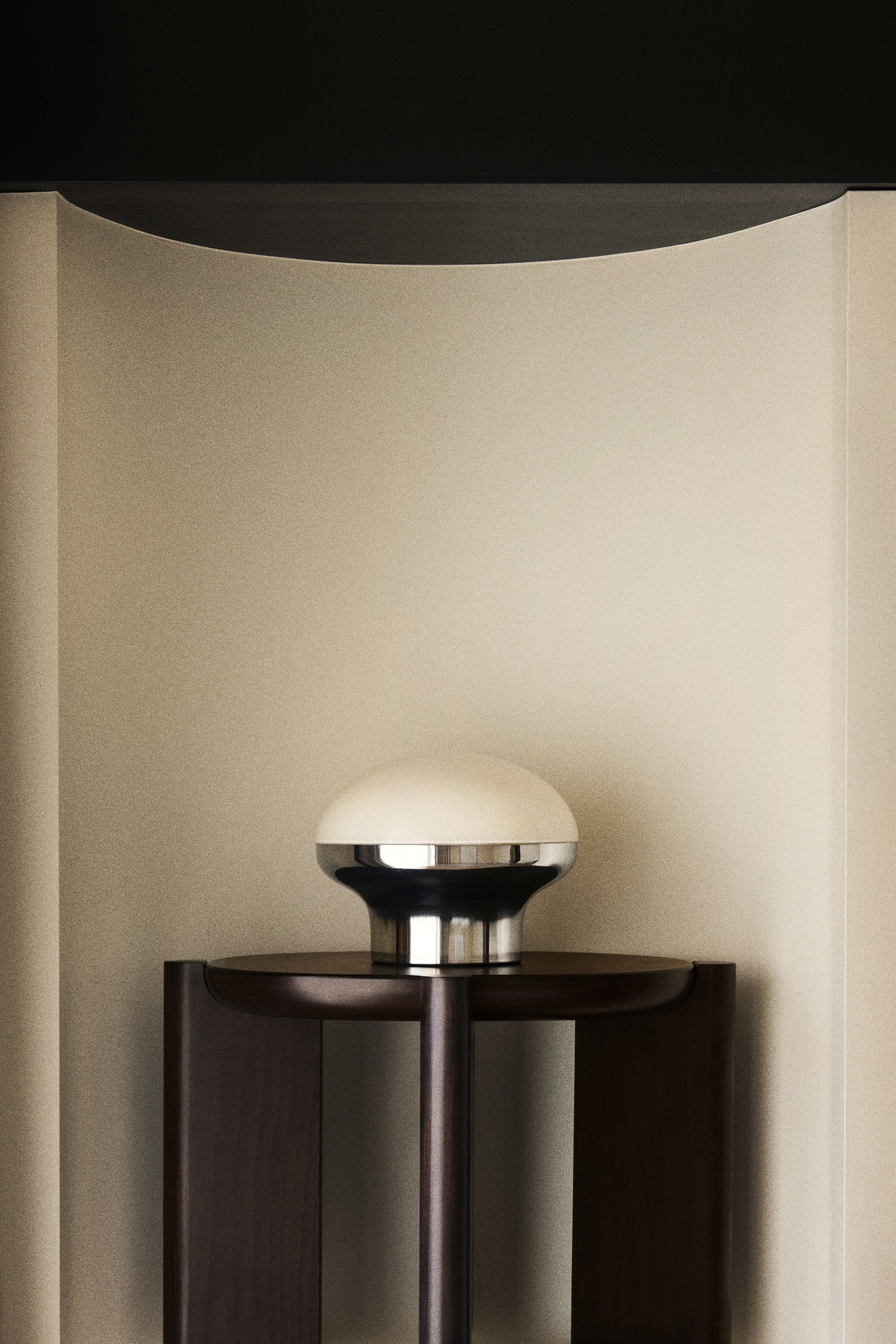 De lamp is ontworpen met een crèmekleurige, koepelvormige kap en een reflecterende, bolvormige chromen voet. Een wit snoer loopt vanuit de linkerkant van de voet.