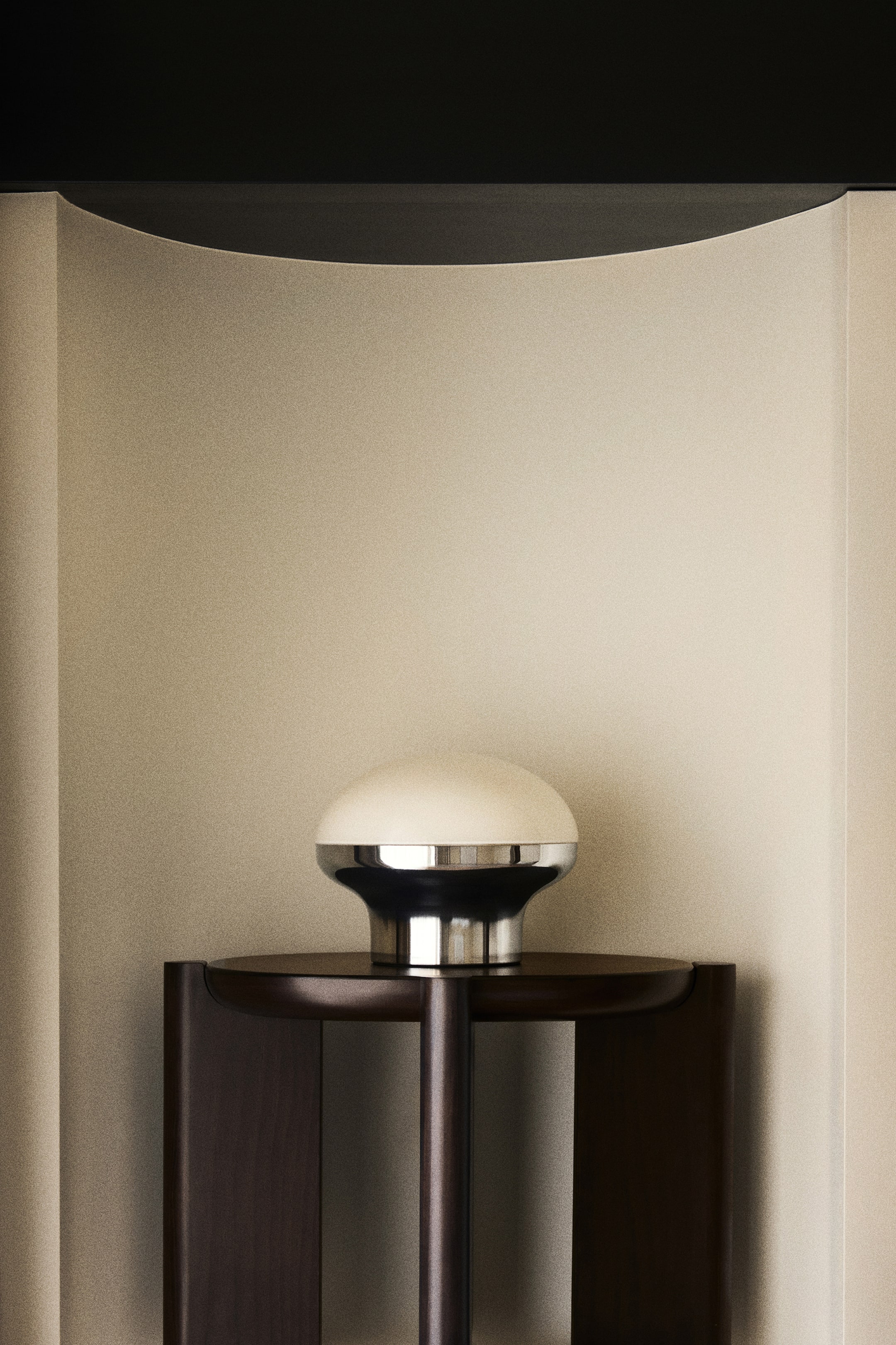 Größeres Bild anzeigen: Eine Tischlampe zeigt einen polierten Metallsockel, der einen kuppelförmigen, transluzenten Glasdiffusor trägt und nach vorne ausgerichtet ist.