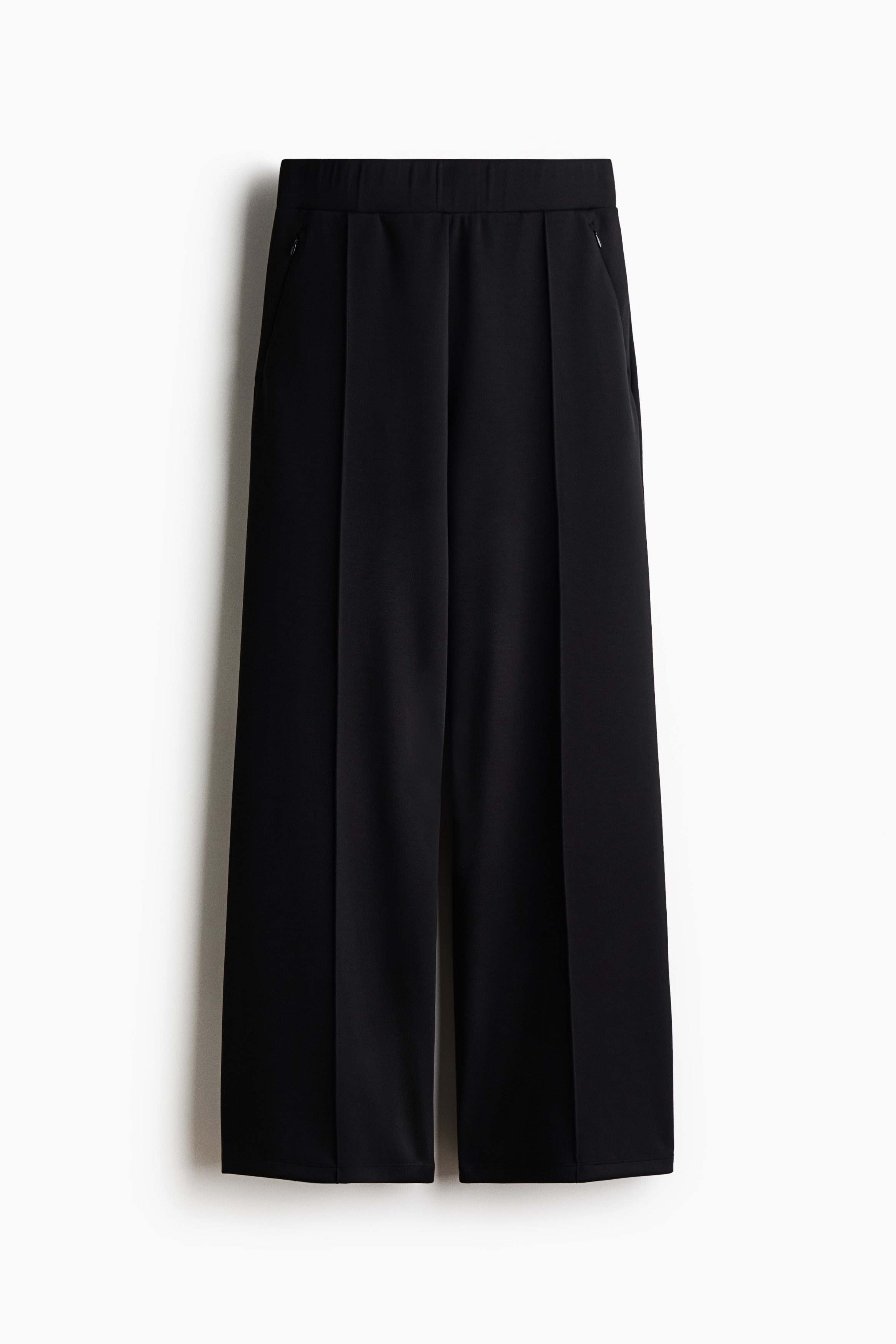Modellen bär Cooling Relaxed Fit Wide byxor. De svarta byxorna har en avslappnad, vid silhuett med en synlig framsöm på varje ben, och modellen placerar en hand i en ficka.