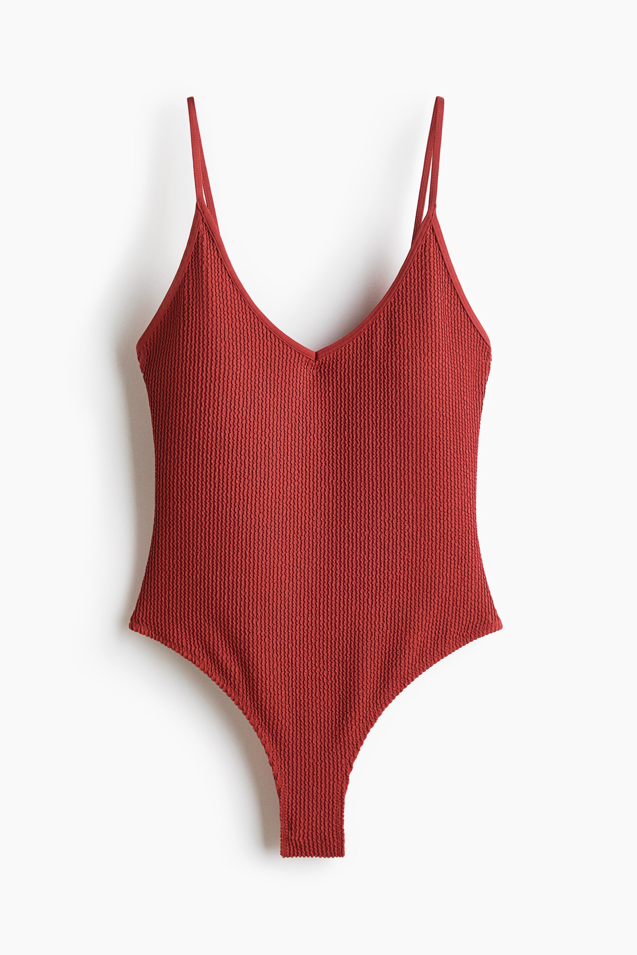 View larger image: A red-orange swimsuit shows a textured jersey fabric and a V-neckline at the front. It features thin, adjustable shoulder straps and high-cut leg openings.