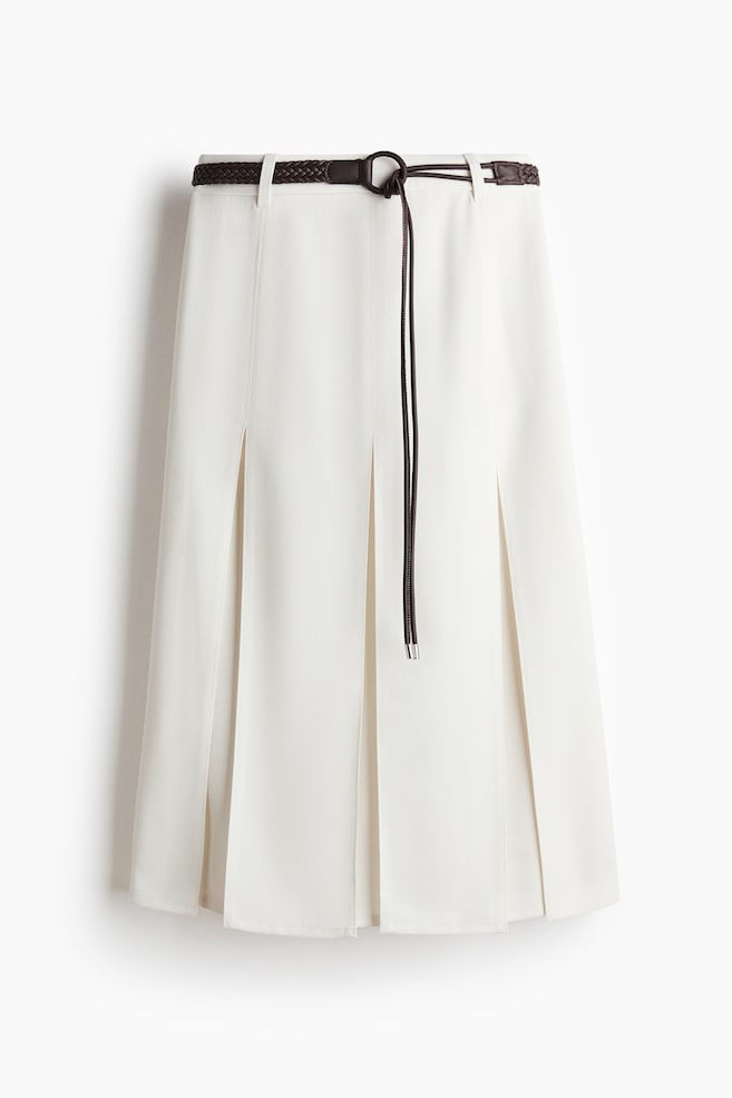 The off-white skirt is featuring a flat waistband with belt loops and multiple vertical pleats on the front. A dark brown braided belt is threaded through the loops, with a long cord hanging down the front. - 1