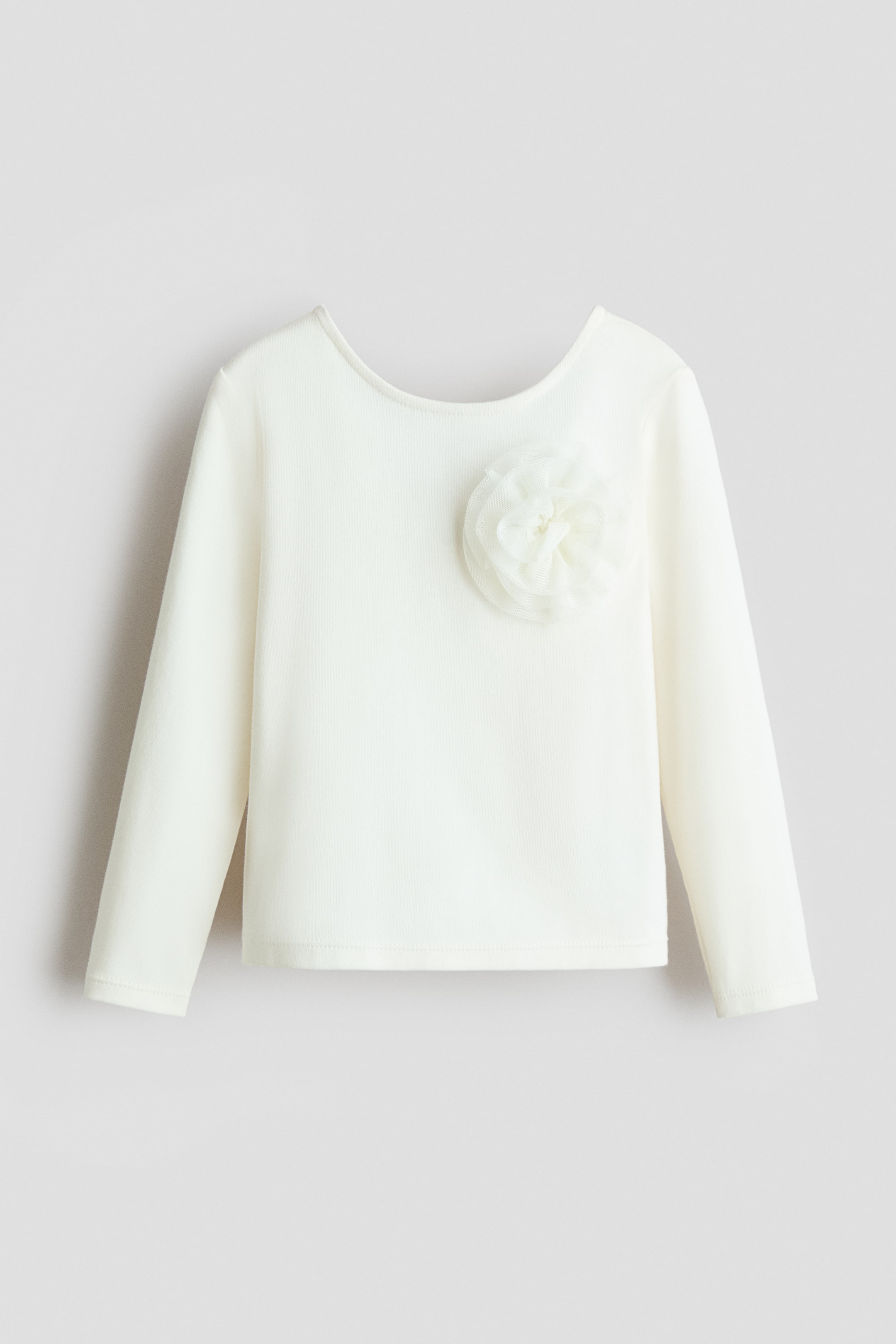 הצגת תמונה גדולה יותר: חולצה ארוכת שרוולים בצבע לבן-חלב מציגה קדימה, עם מחשוף עגול מעט מעוגל. פרח מבד בשכבות מוסיף עיטור באזור החזה השמאלי.