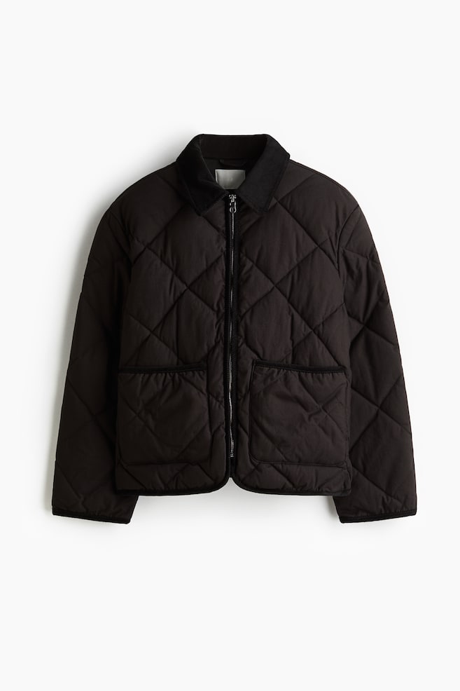 A lightly padded jacket is displayed FRONT, crafted in quilted cotton canvas and featuring a corduroy collar. It is detailed with a zip down the front, two patch front pockets, gently dropped shoulders, and long sleeves. - 1