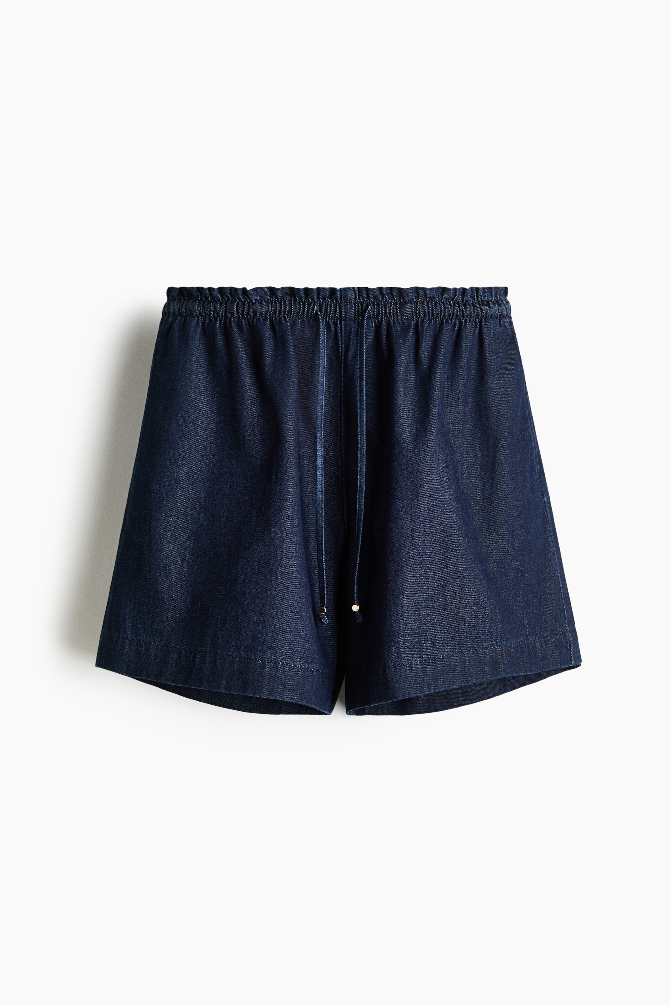 View larger image: Loose-fit shorts in lightweight denim crafted from a cotton and lyocell blend are showcased from the front. They boast a high, elasticated waist adorned with a subtle frill trim, a slender drawstring embellished with metal beads, and discreet side pockets.