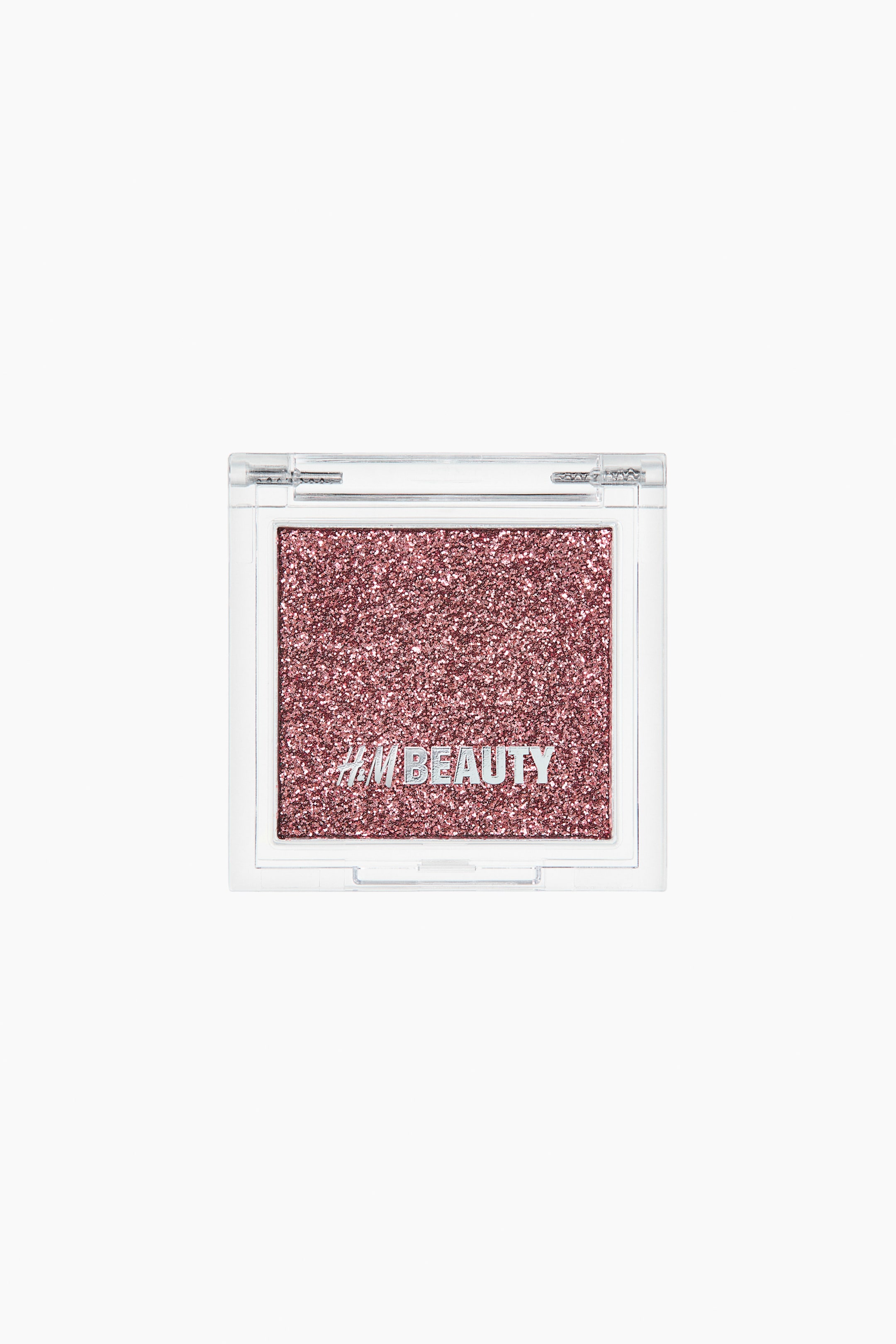 Zobacz większy obraz: Cień do powiek. Prostokątne, przezroczyste plastikowe opakowanie zawiera sprasowany cień do powiek w kolorze różowego złota z brokatem, na którego powierzchni widnieje srebrny napis "H&M BEAUTY".