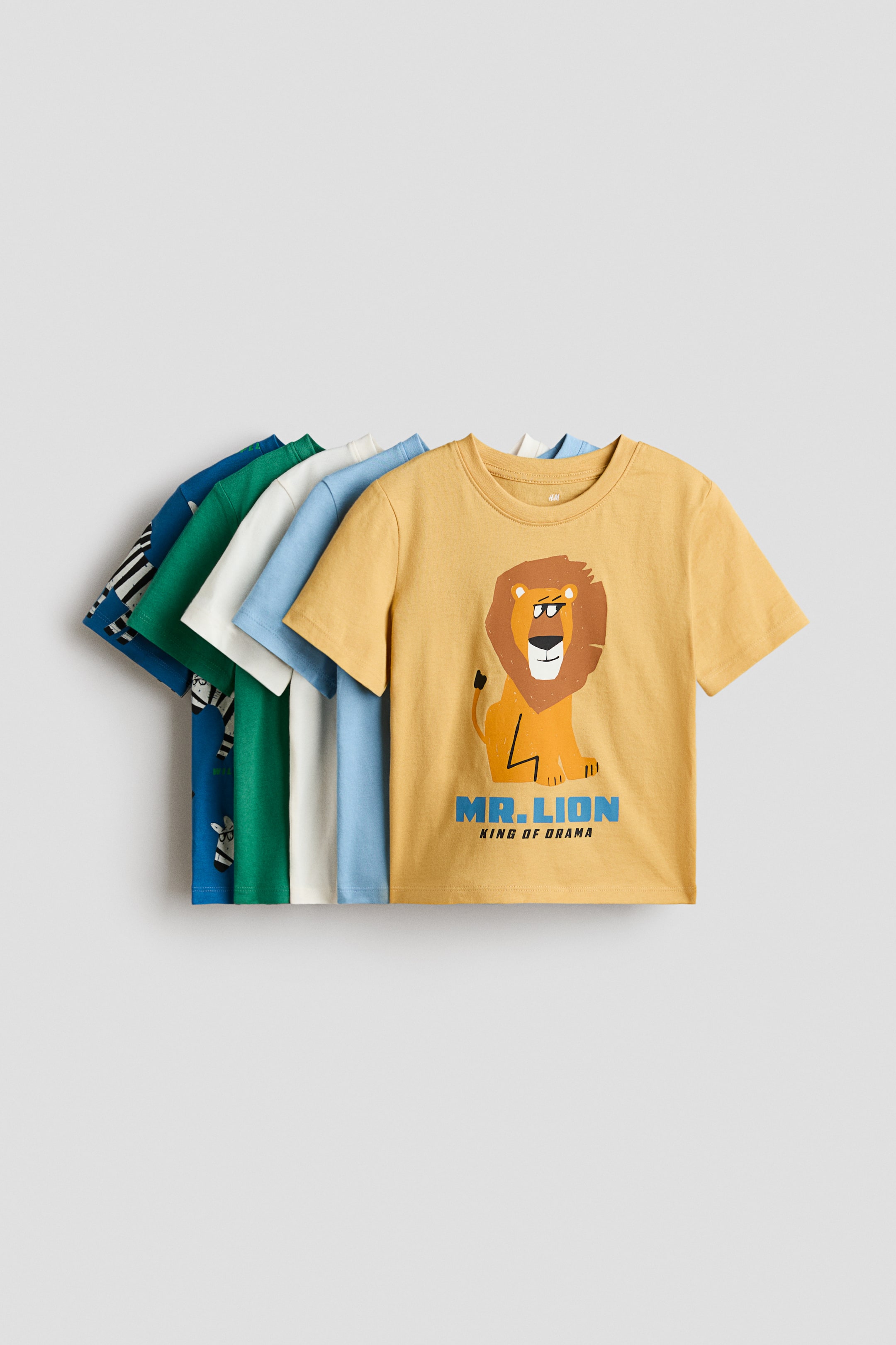 View larger image: Classic T-shirts in soft cotton jersey are neatly displayed, each featuring a round, ribbed neckline. The front T-shirt is mustard yellow with a cartoon lion print, while the others in the background are in light blue, white, green, and dark blue.