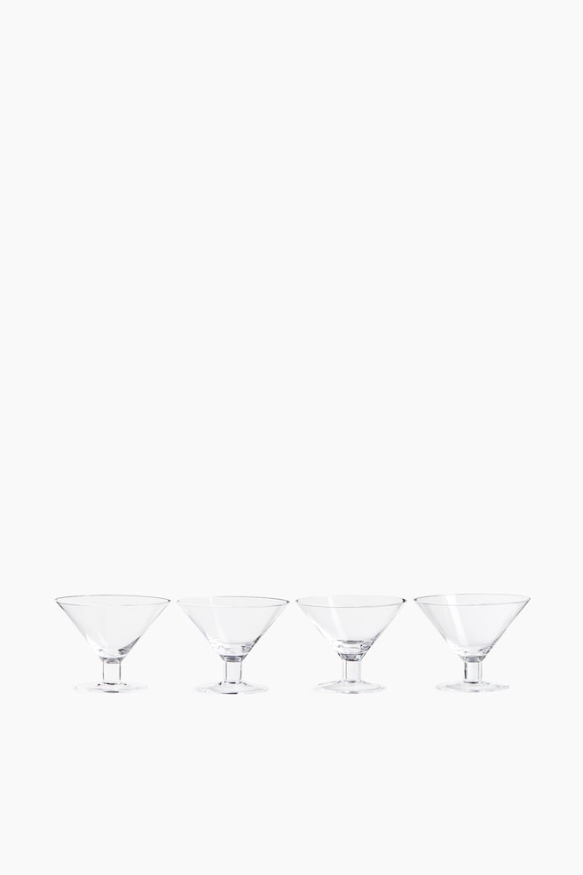 Four clear cocktail glasses are standing in a row from a front view, showcasing their wide, conical bowls. Each glass features a very short, thick cylindrical stem and a flat, circular base. - 1