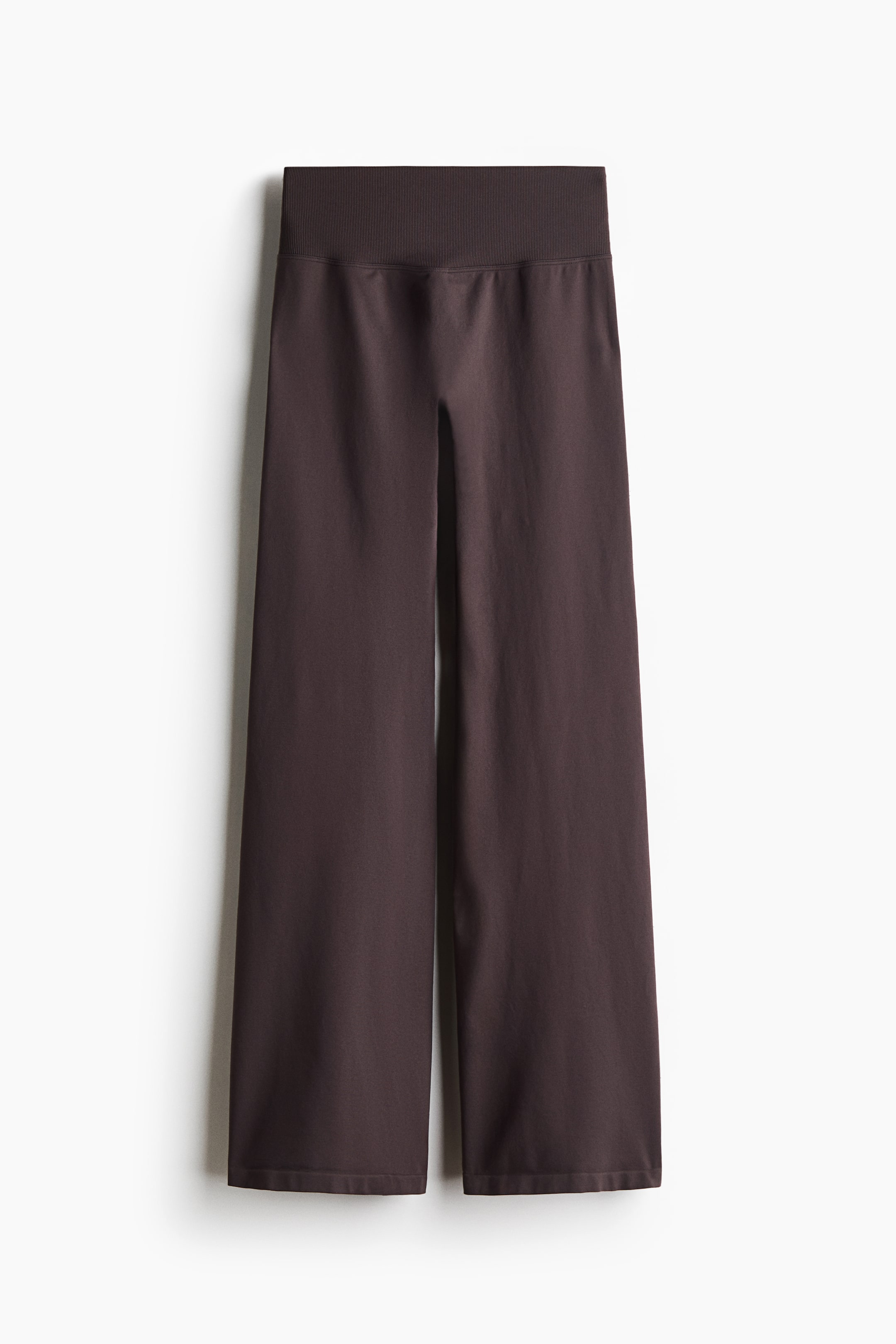 View larger image: These dark brown wide-leg knit trousers are hanging in a front view, showcasing a high-rise, wide elasticated waistband and a relaxed, seamless silhouette.