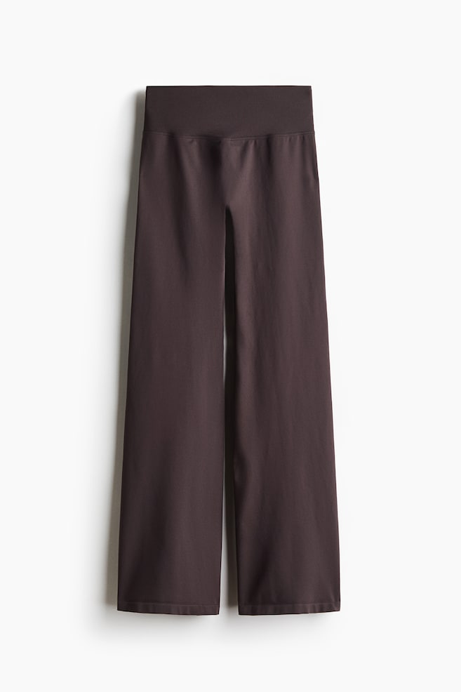 These dark brown wide-leg knit pants are hanging from a front view, showcasing a high-rise, wide elasticized waistband and a relaxed, seamless silhouette. - 1