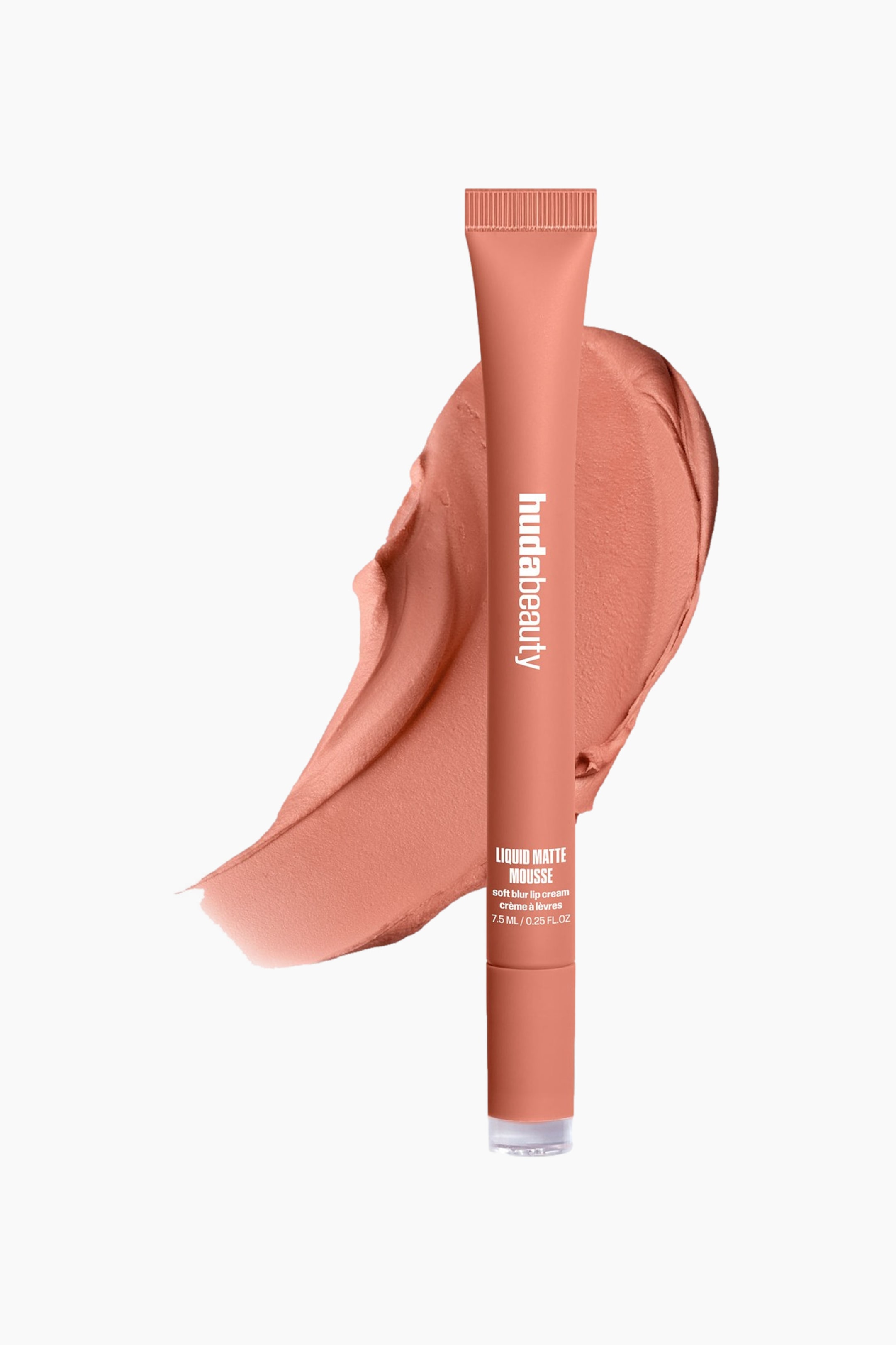 Visa större bild: Den persikotonade Huda Beauty Liquid Matte Mousse-tuben står lätt vinklad åt höger och har ett räfflat lock samt en transparent bas. Den visar ”hudabeauty” vertikalt och ”LIQUID MATTE MOUSSE soft blur lip cream crème à lèvres 7.5 ML / 0.25 FL.OZ” horisontellt, medan den vilar på ett texturerat prov av den matchande persikotonade nude-moussen.