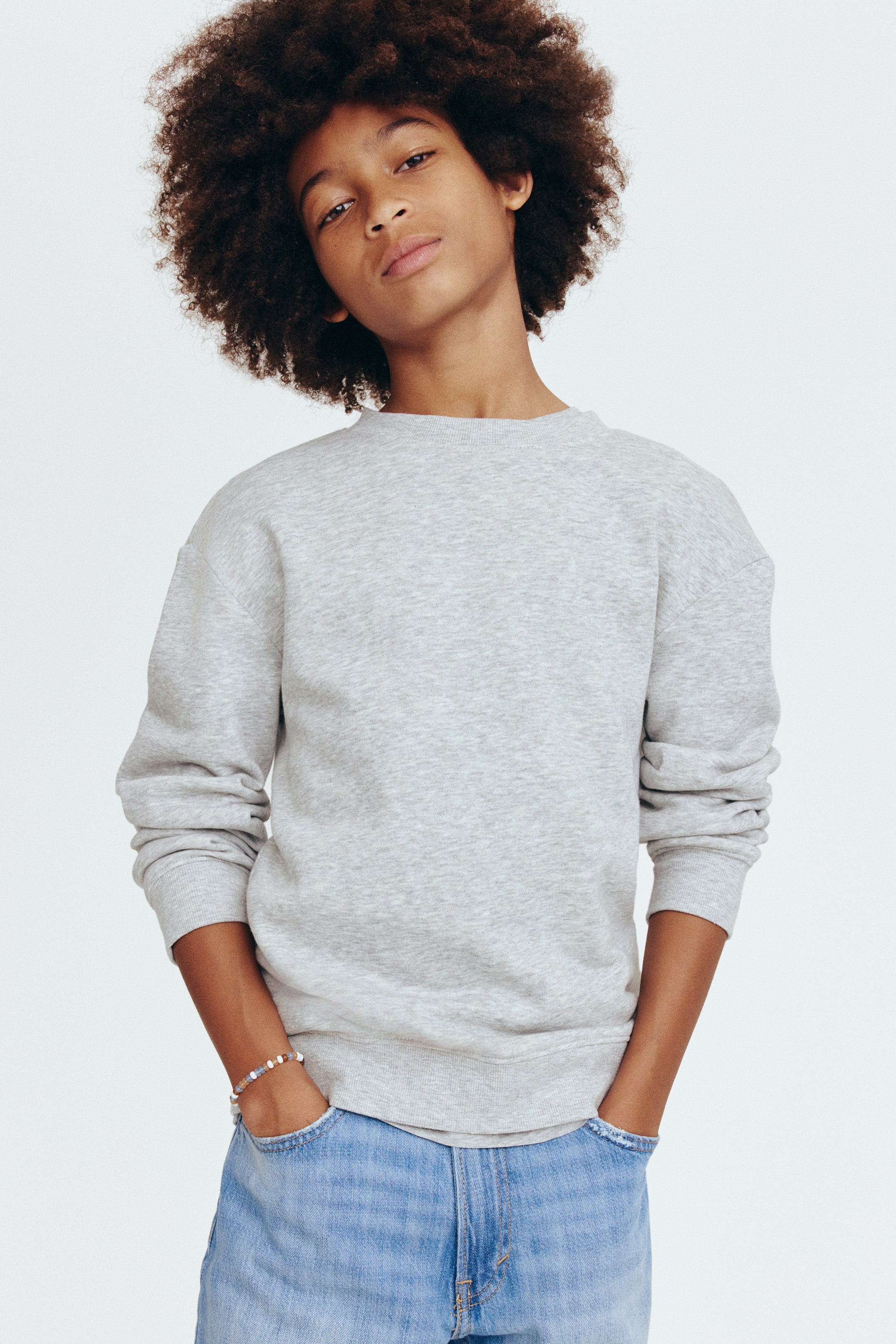 View larger image: A light gray crew neck sweatshirt is showcased, featuring a ribbed neckline, ribbed cuffs, and a ribbed hem. It's styled with light wash blue jeans, highlighting the visible front pockets and frayed top edges.