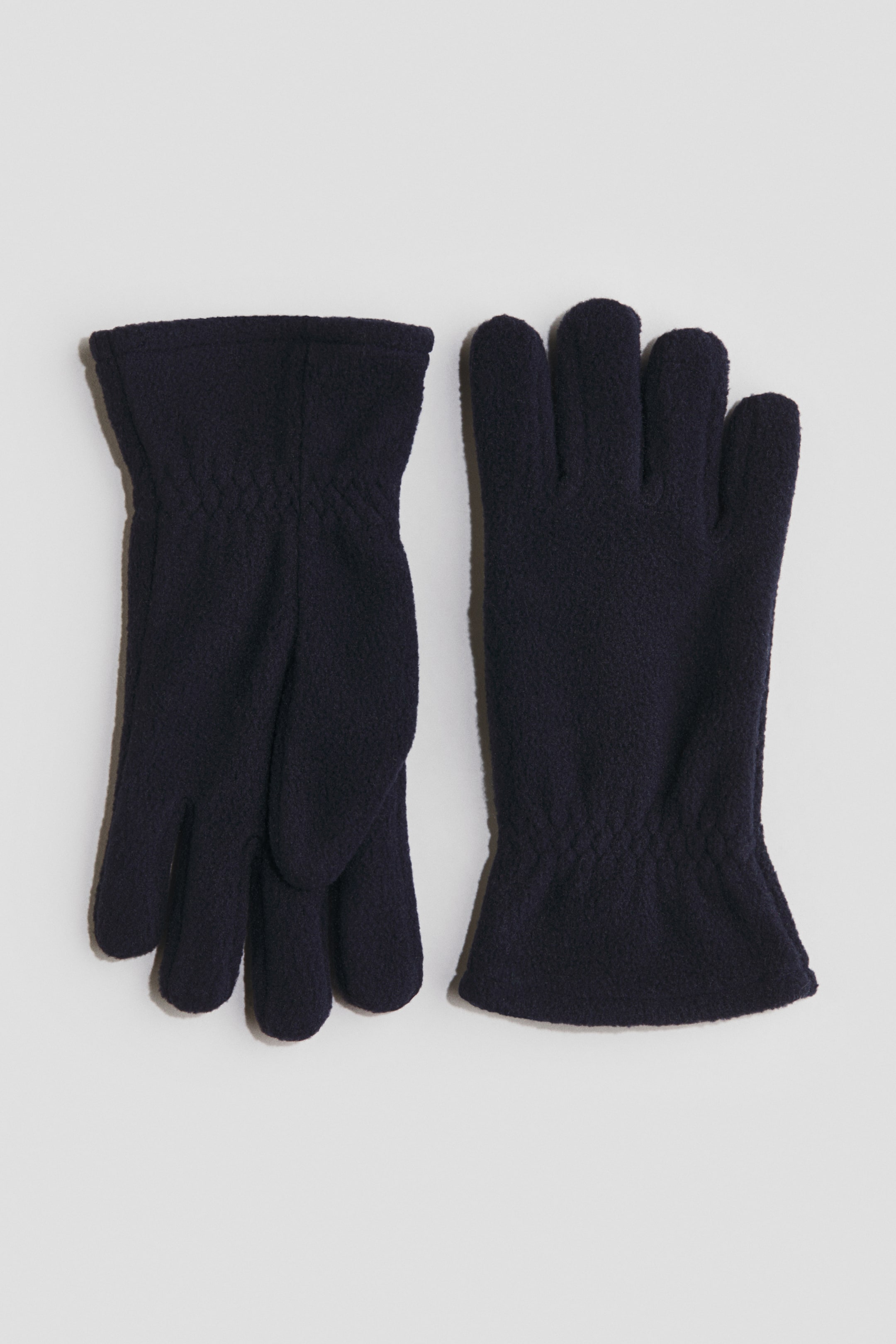 Ampliar la imagen: Un par de guantes de forro polar azul oscuro está colocado en posición horizontal, cada uno con cinco dedos y elástico en las muñecas.