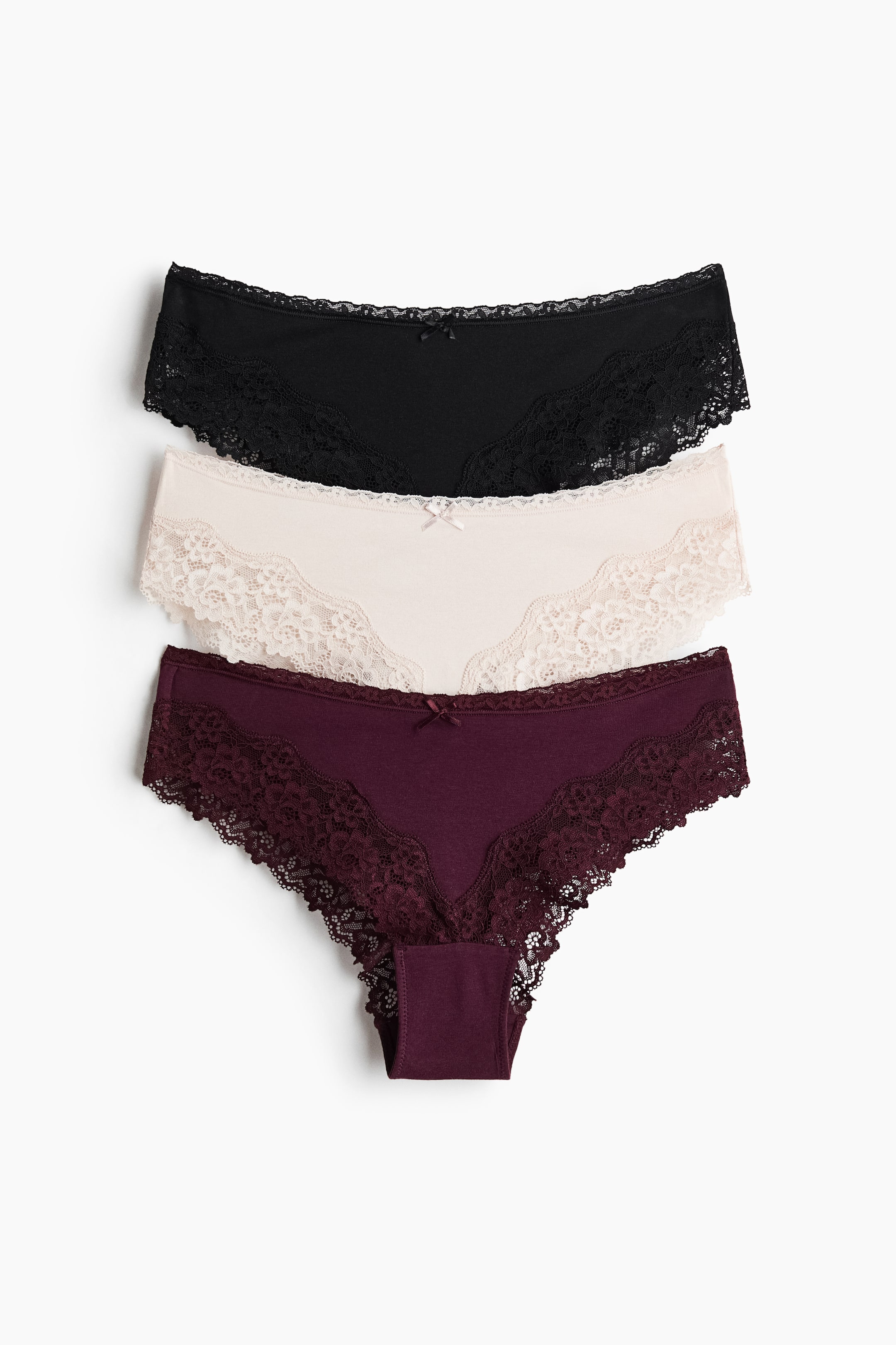 Ver imagen más grande: Tres pares de braguitas están superpuestas, mostrando sus vistas frontales en colores negro, beige claro y burdeos. Cada braguita de cintura media está hecha de jersey de algodón y presenta un delicado ribete de encaje a lo largo de las cinturas y las aberturas de las piernas, con un pequeño lazo adornando su parte central delantera.