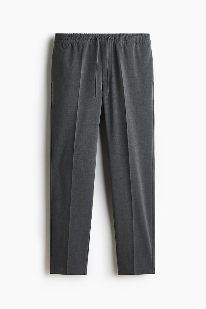 Dark gray tailored joggers are featuring a woven fabric, covered elastication with a drawstring at the waist, a smooth front with side pockets, and sharp creases running down the front of the legs, presenting a slim fit silhouette. - 1