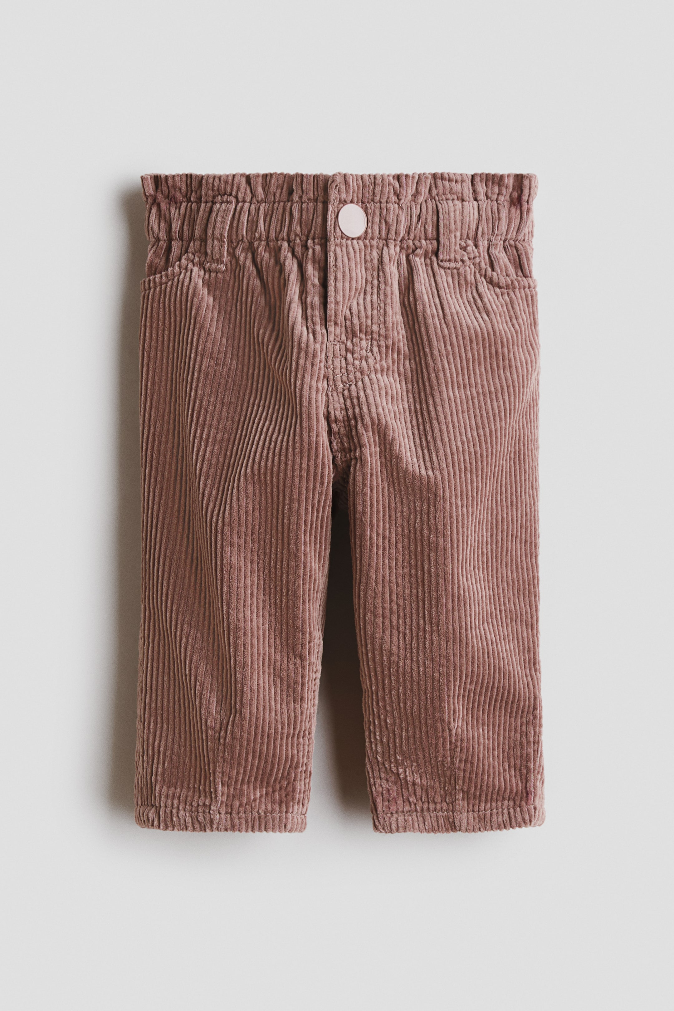 View larger image: A pair of mauve corduroy trousers is displayed front-facing, featuring an elasticated, gathered waistband with belt loops and a light pink round button securing the centre front above a stitched fly. Two side slash pockets are visible, and the trousers are showcasing a full-length, straight-leg cut with a finished hem.