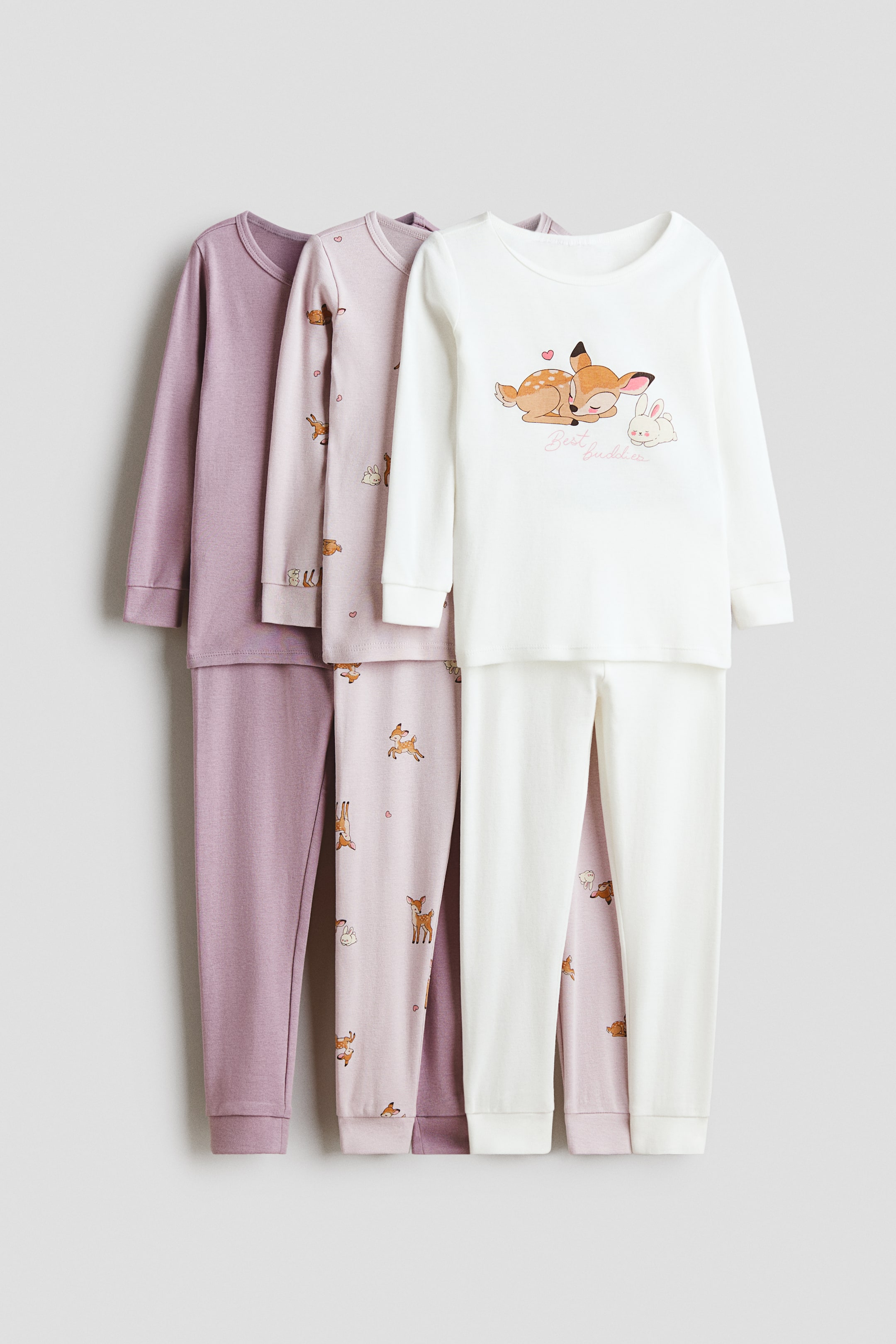 View larger image: A three-pack of slim-fit cotton pajamas is shown in three front-facing sets. The white set features a long-sleeved top with a sleeping deer and rabbit graphic, paired with solid white long pants. Behind it, a light pink set with an all-over deer and rabbit pattern and a solid purple set are displayed, both with crew necklines, long sleeves, and matching long pants.