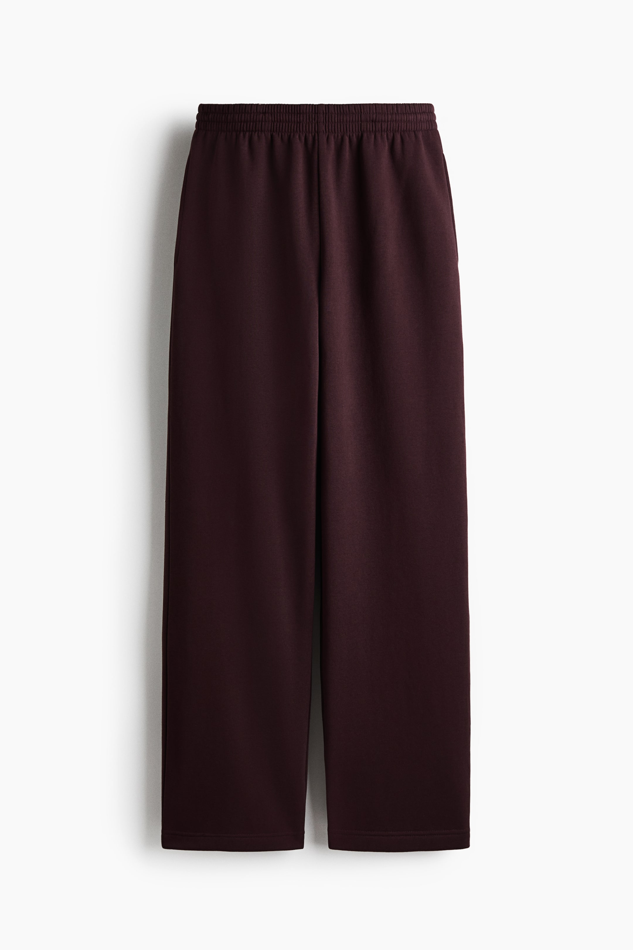 View larger image: Dark burgundy track pants are shown in a front view, featuring a wide elasticized smocked waistband and straight-cut legs. The pants offer a relaxed, structured fit with clean, simple hems.