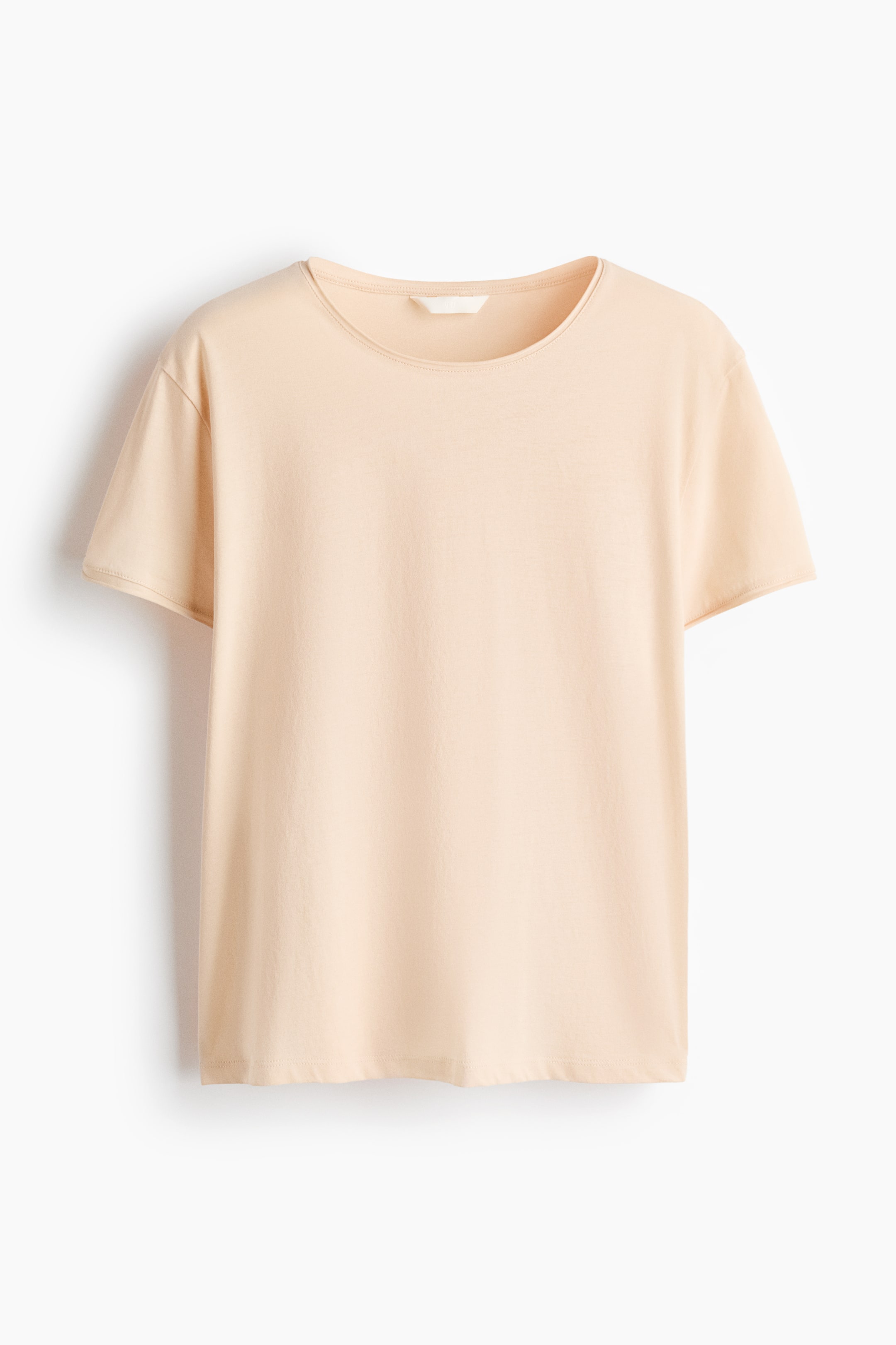 View larger image: A light peach t-shirt is shown from the front, showcasing a round neckline with a narrow band and short sleeves. A small white tag can be seen at the back of the neckline.