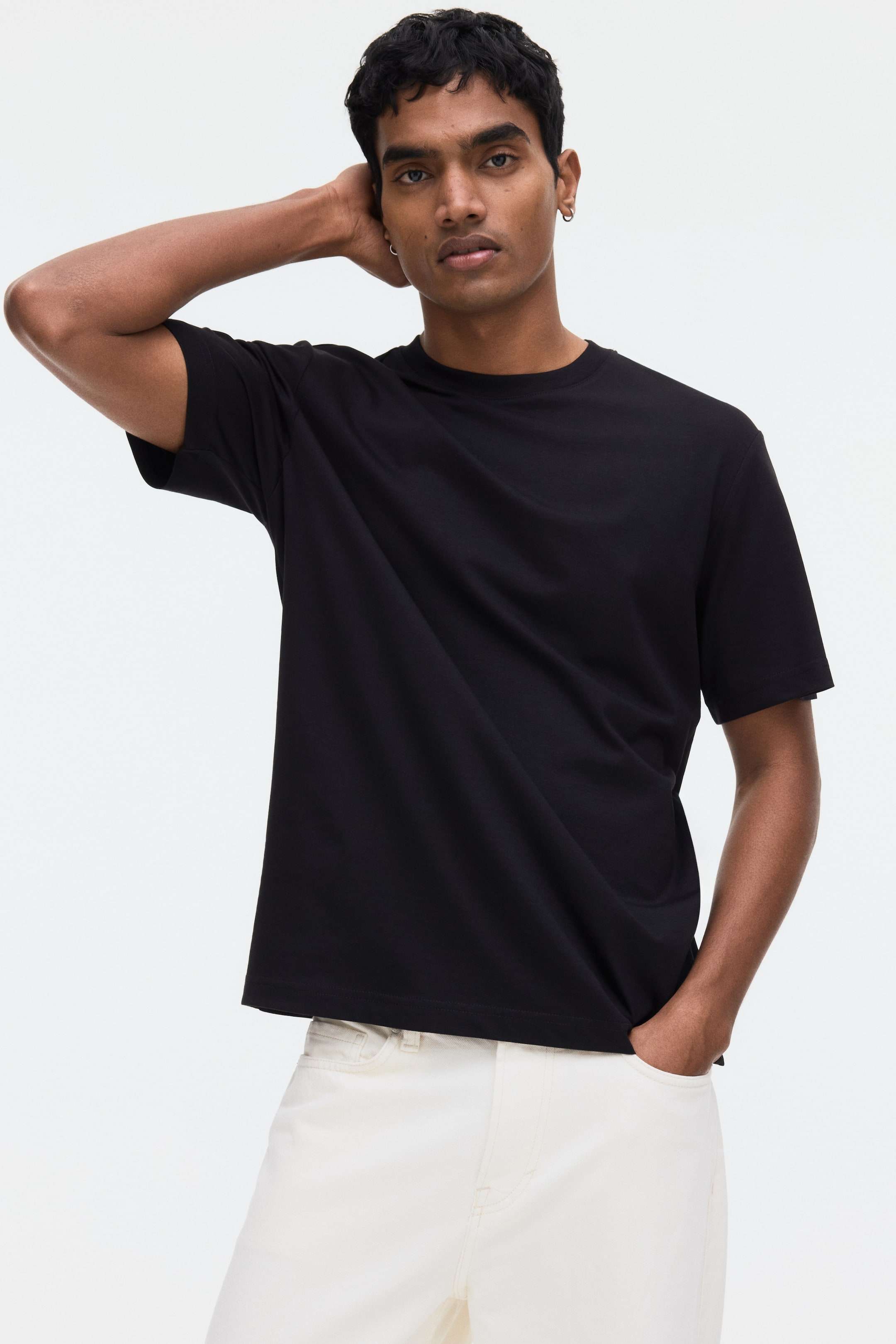 Ver imagen más grande: Una camiseta negra que presenta un cuello redondo y mangas cortas. Ofrece una textura de tela suave y un ajuste relajado, con un dobladillo recto visible.
