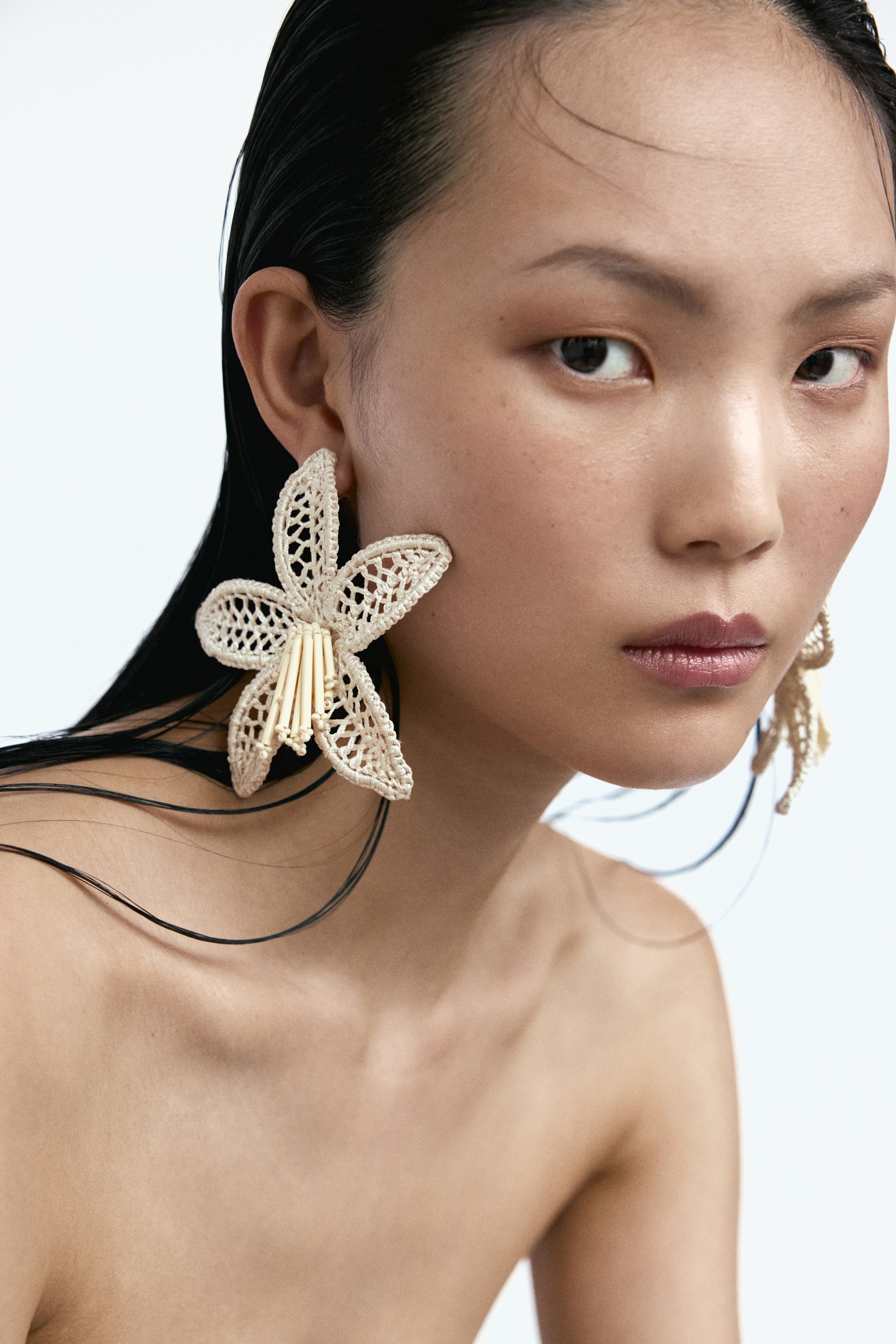 Grotere afbeelding bekijken: Bloemvormige oorbellen met een gehaakte look en glazen buiskralen in het midden worden gedragen door het model. Eén oorbel is zichtbaar aan het rechteroor van het model.
