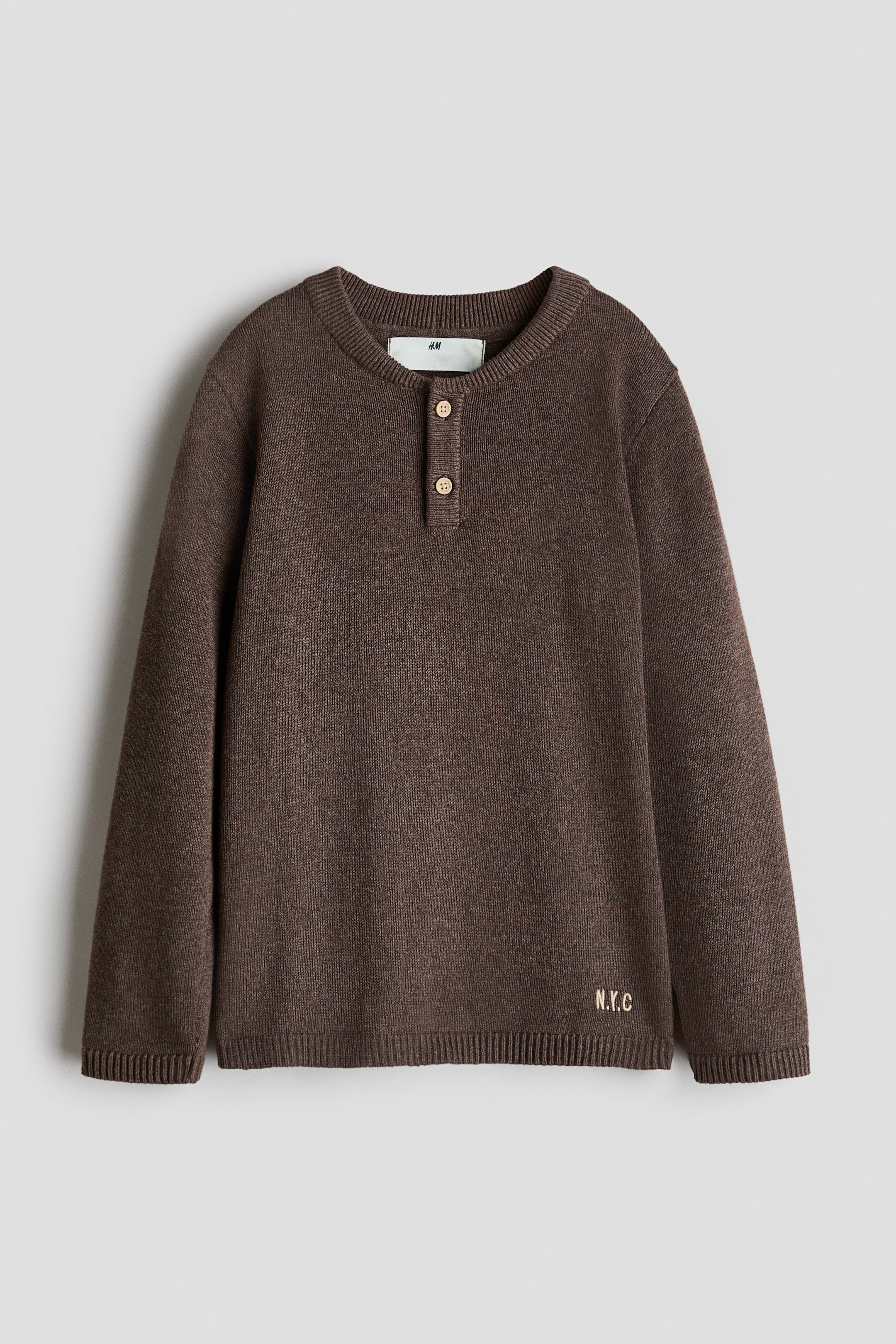 View larger image: A brown waffle-knit sweater is shown from the front, featuring a ribbed henley collar with three light brown buttons. It is designed with dropped shoulders, ribbed cuffs, and a ribbed hem, with 'N.Y.C' embroidered in light gold on the lower right front.