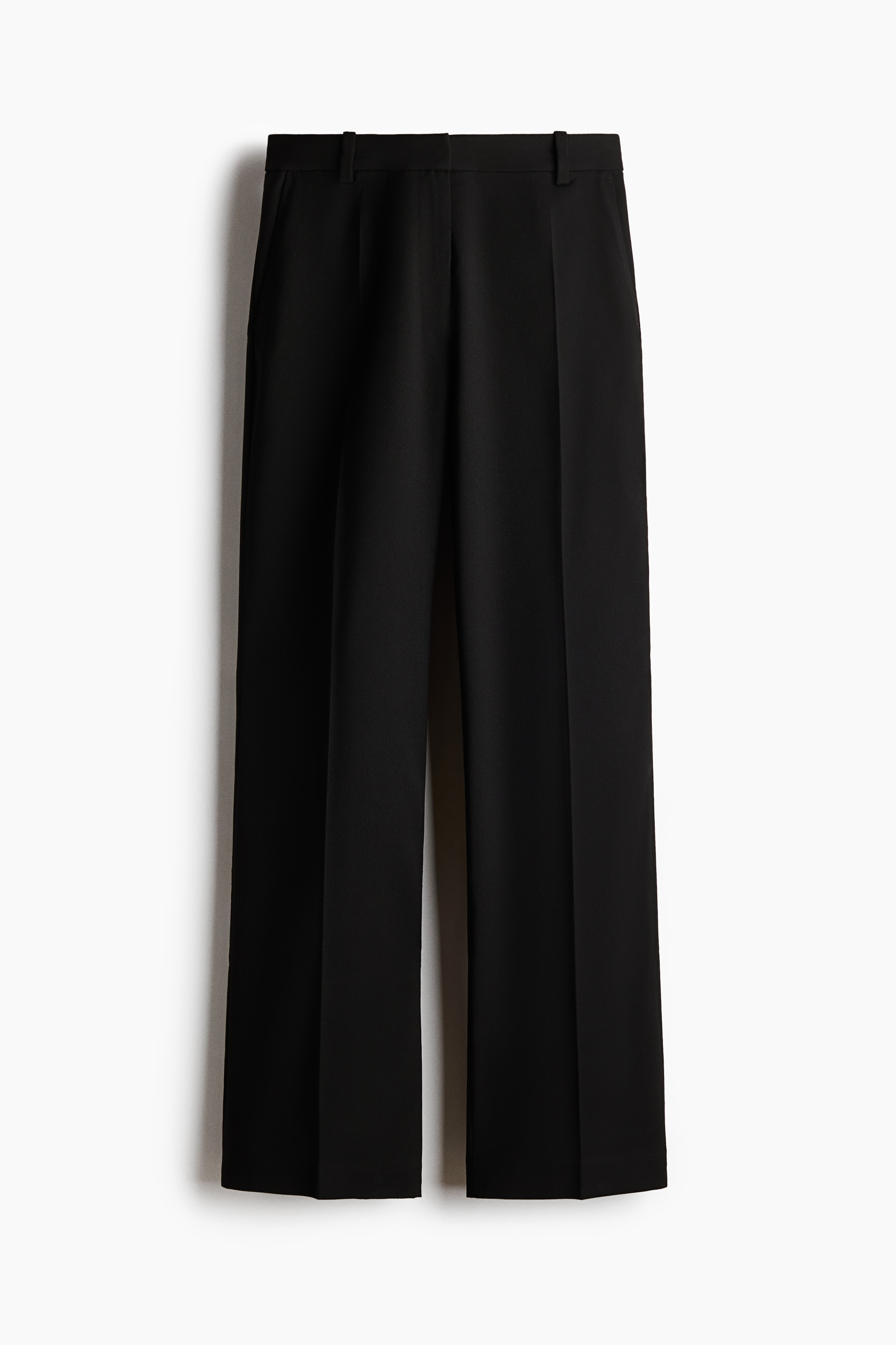 Schwarze, maÃgeschneiderte Hosen werden von vorne gezeigt und zeichnen sich durch eine strukturierte Passform mit Bootcut-Beinen und scharfen BÃ¼gelfalten entlang der Mitte jedes Beins aus. Die Hose ist mit einem oversized schwarzen Blazer, einem schwarzen Spitzentop aus Spitze und schwarzen Pumps mit spitzer Zehenpartie kombiniert.